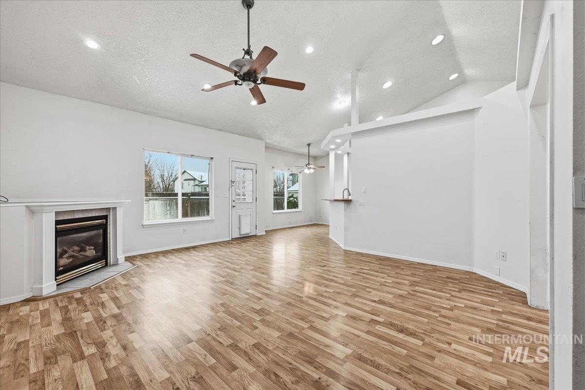 Unfurnished living room featuring ceiling fan, recessed lighting, gas corner fireplace, light wood-type flooring, Smart lights/switches and vaulted ceiling