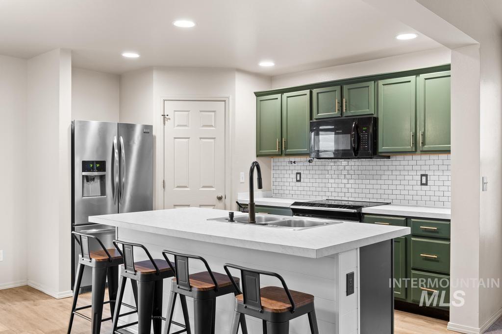 Kitchen featuring green cabinetry, a kitchen bar, light countertops, black appliances, and light wood-style flooring