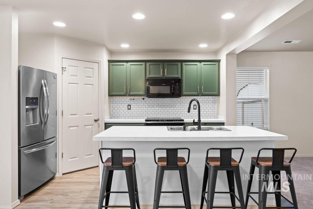 Kitchen featuring green cabinetry, stainless steel fridge with ice dispenser, light countertops, tasteful backsplash, and black microwave