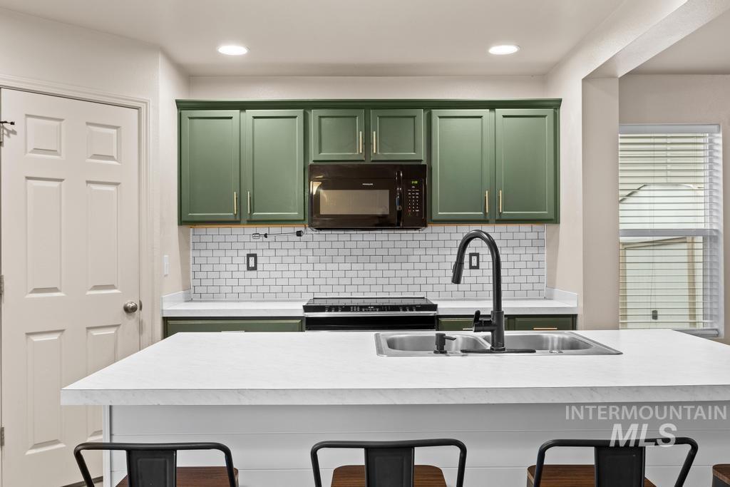 Kitchen featuring green cabinets, a kitchen breakfast bar, black microwave, light countertops, and recessed lighting