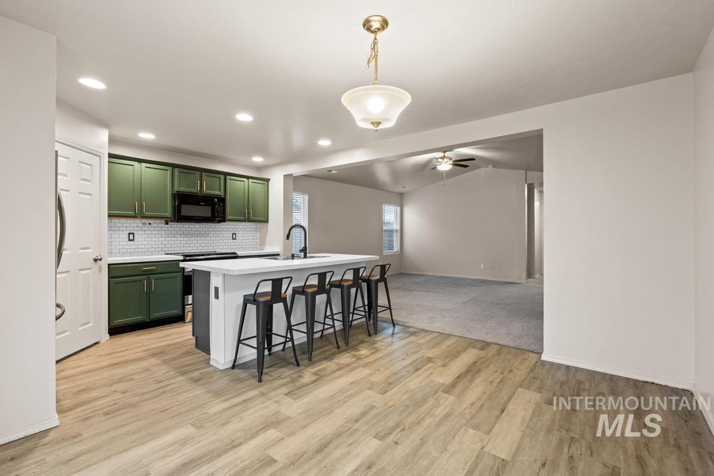 Kitchen with green cabinets, a breakfast bar area, open floor plan, stainless steel electric stove, and hanging light fixtures