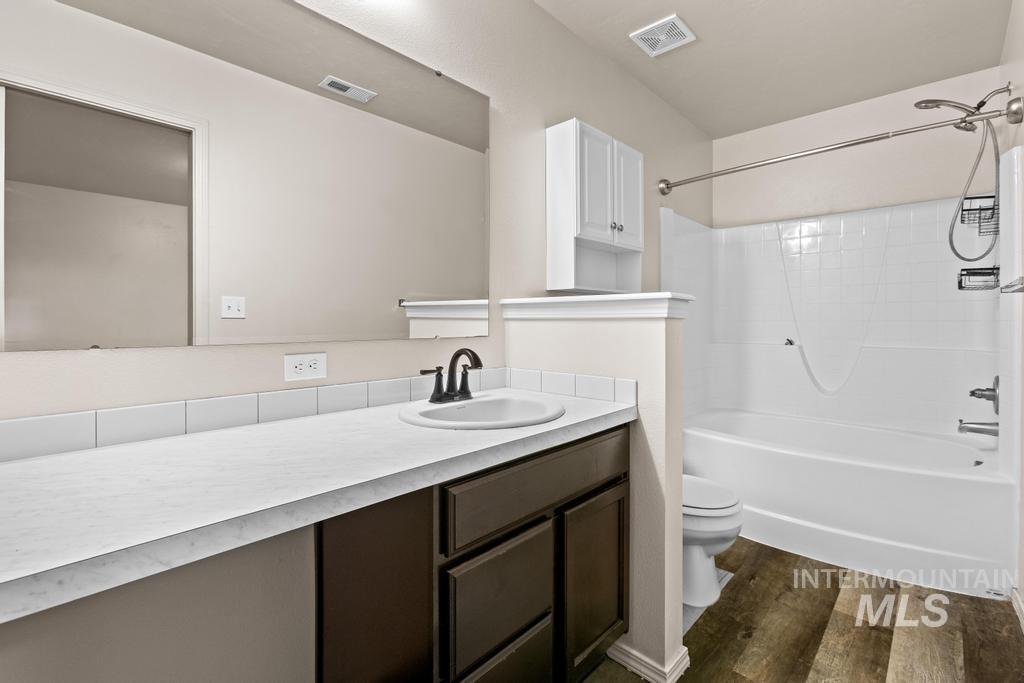 Full bath with washtub / shower combination, vanity, and dark wood-type flooring