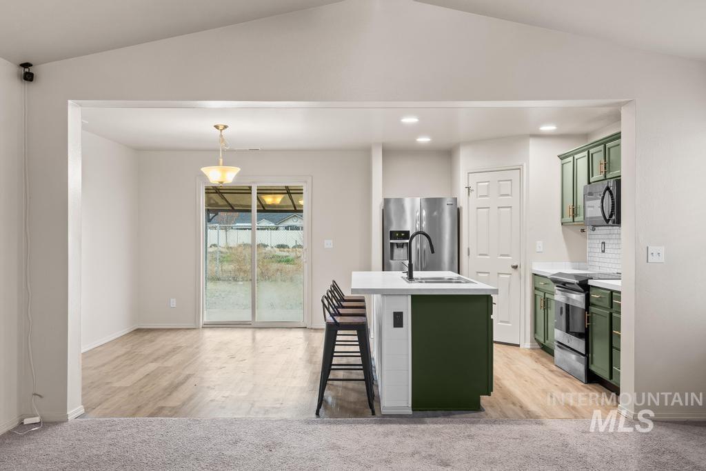 Kitchen featuring green cabinetry, light countertops, appliances with stainless steel finishes, vaulted ceiling, and a kitchen island with sink