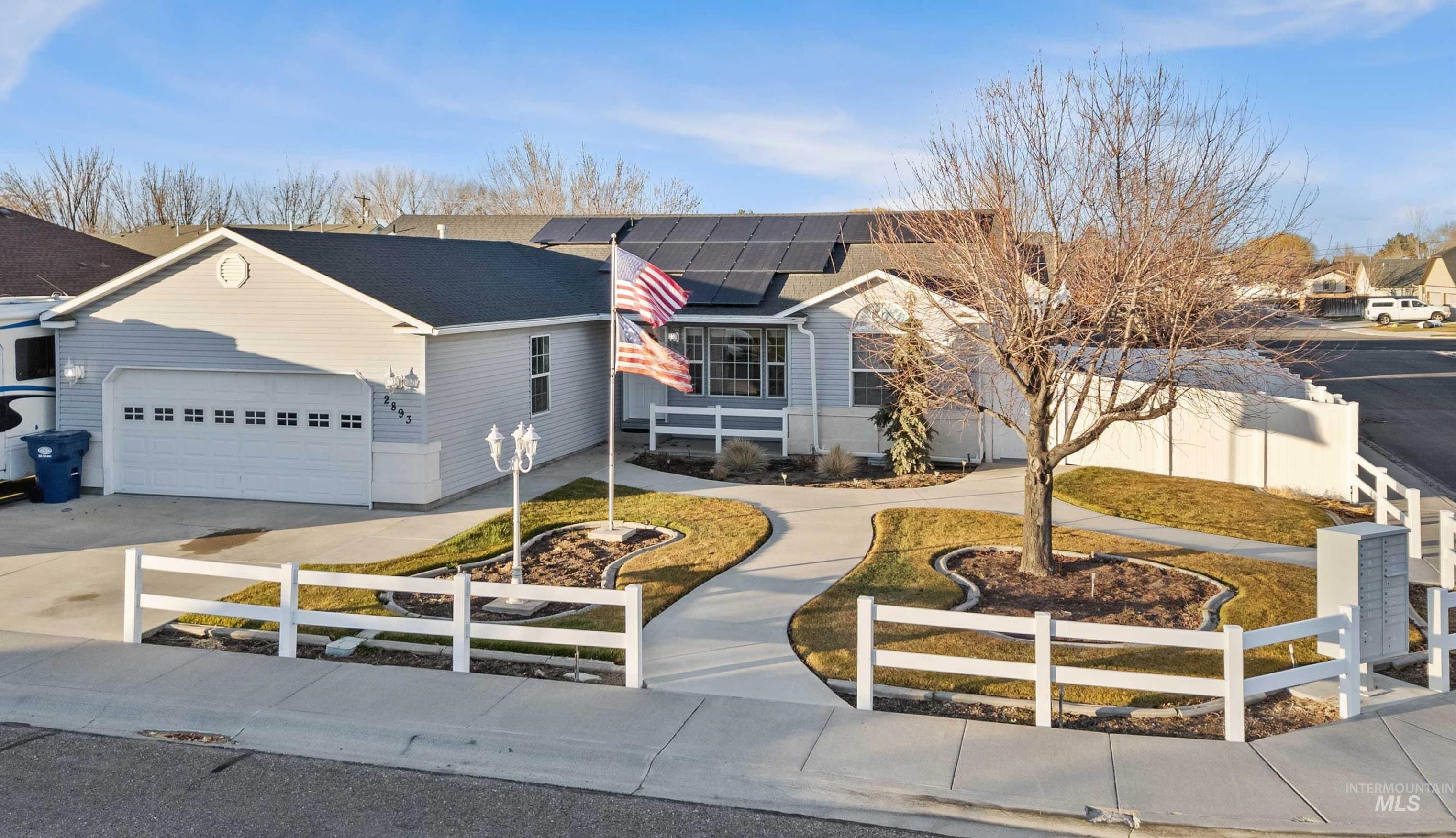 Ranch-style home featuring a fenced front yard, concrete driveway, solar panels, and a garage