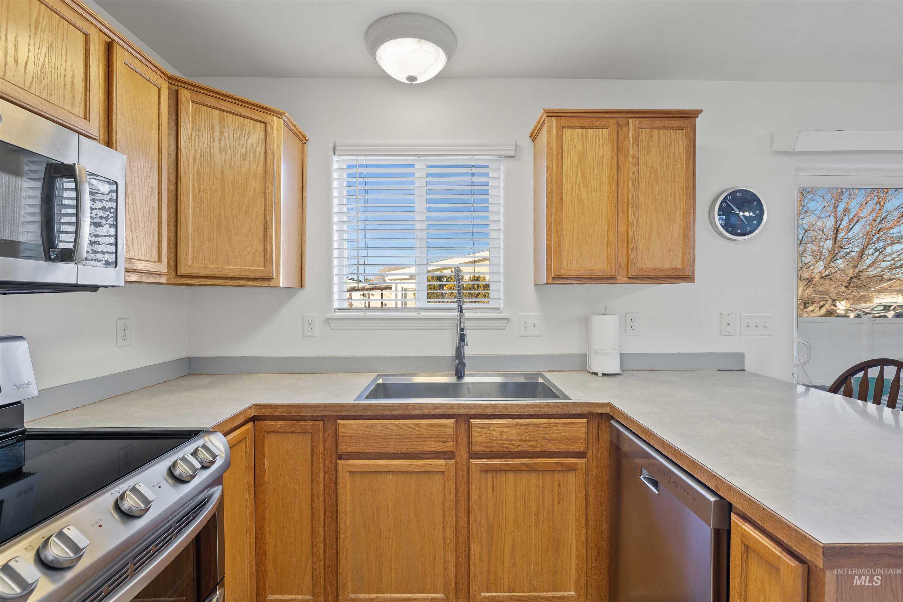 Kitchen with stainless steel appliances, light countertops, a peninsula, and brown cabinetry
