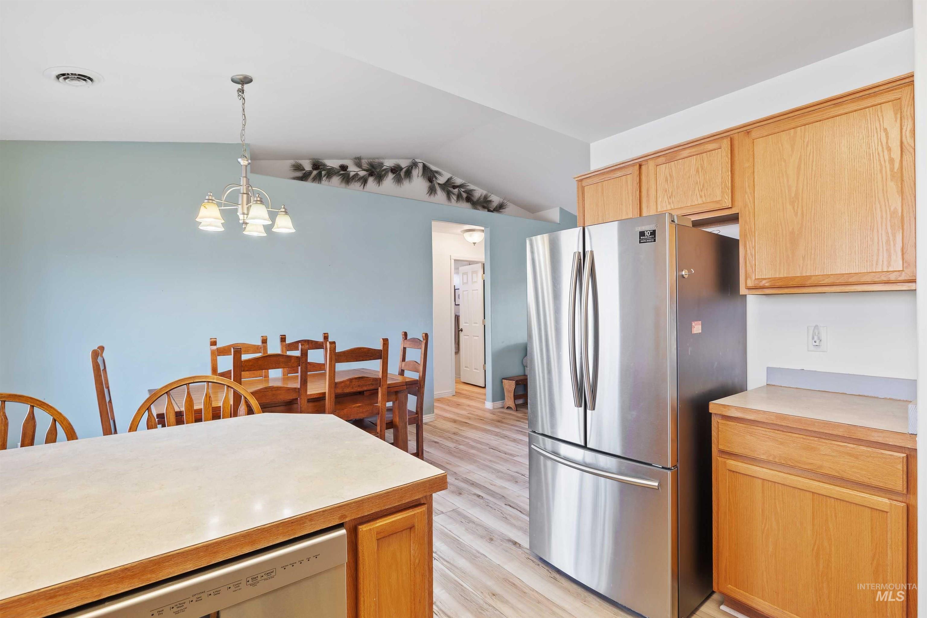 Kitchen with freestanding refrigerator, light countertops, decorative light fixtures, dishwashing machine, and lofted ceiling