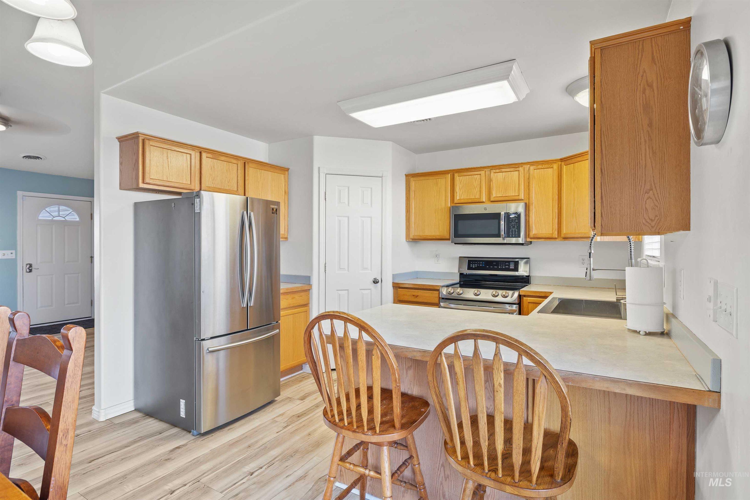 Kitchen with light countertops, appliances with stainless steel finishes, a kitchen bar, a peninsula, and light wood-type flooring