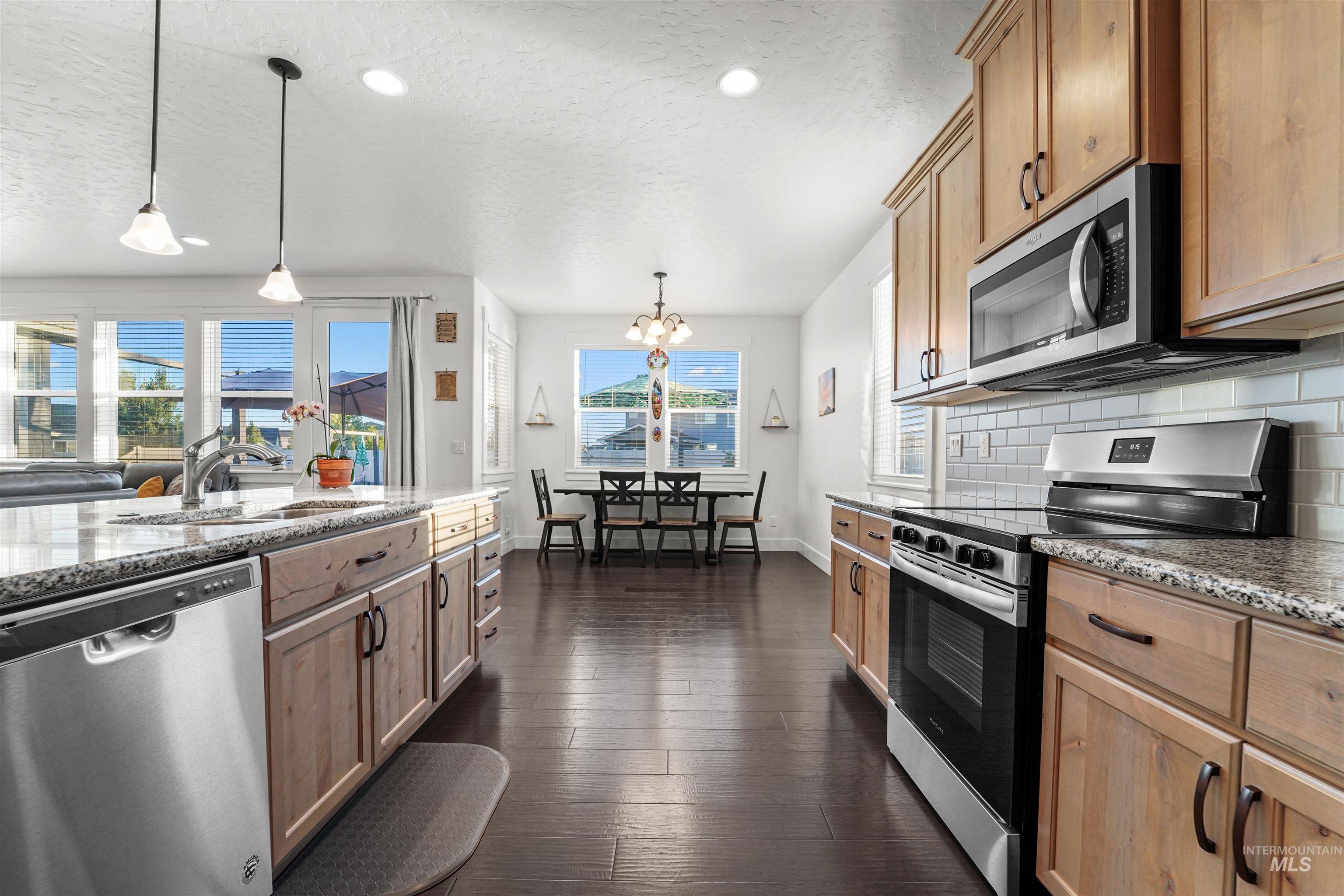 Kitchen with appliances with stainless steel finishes, light stone countertops, pendant lighting, a chandelier, and a textured ceiling