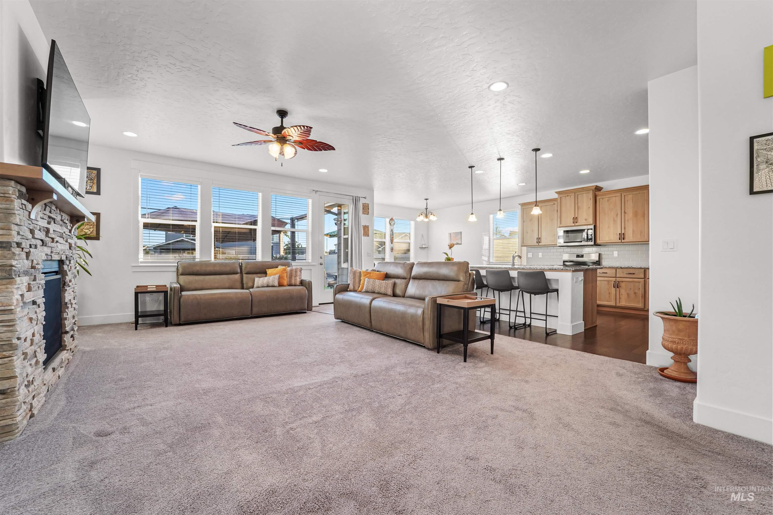 Living room featuring dark colored carpet, a textured ceiling, a ceiling fan, a fireplace, and recessed lighting