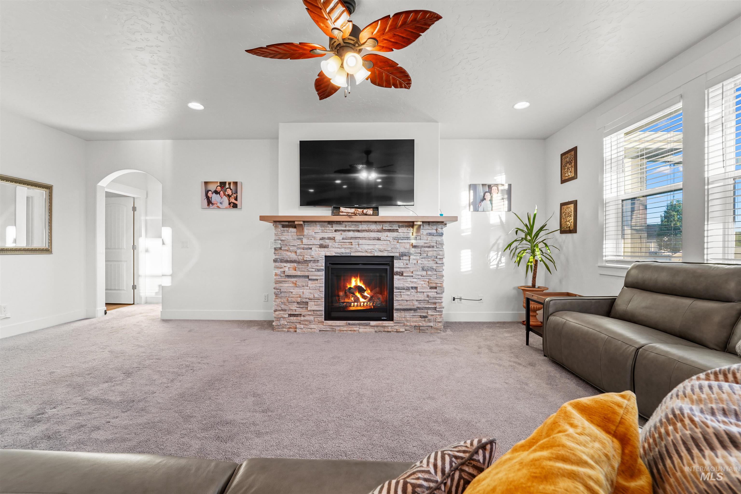 Living area featuring carpet floors, a stone fireplace, arched walkways, ceiling fan, and a textured ceiling