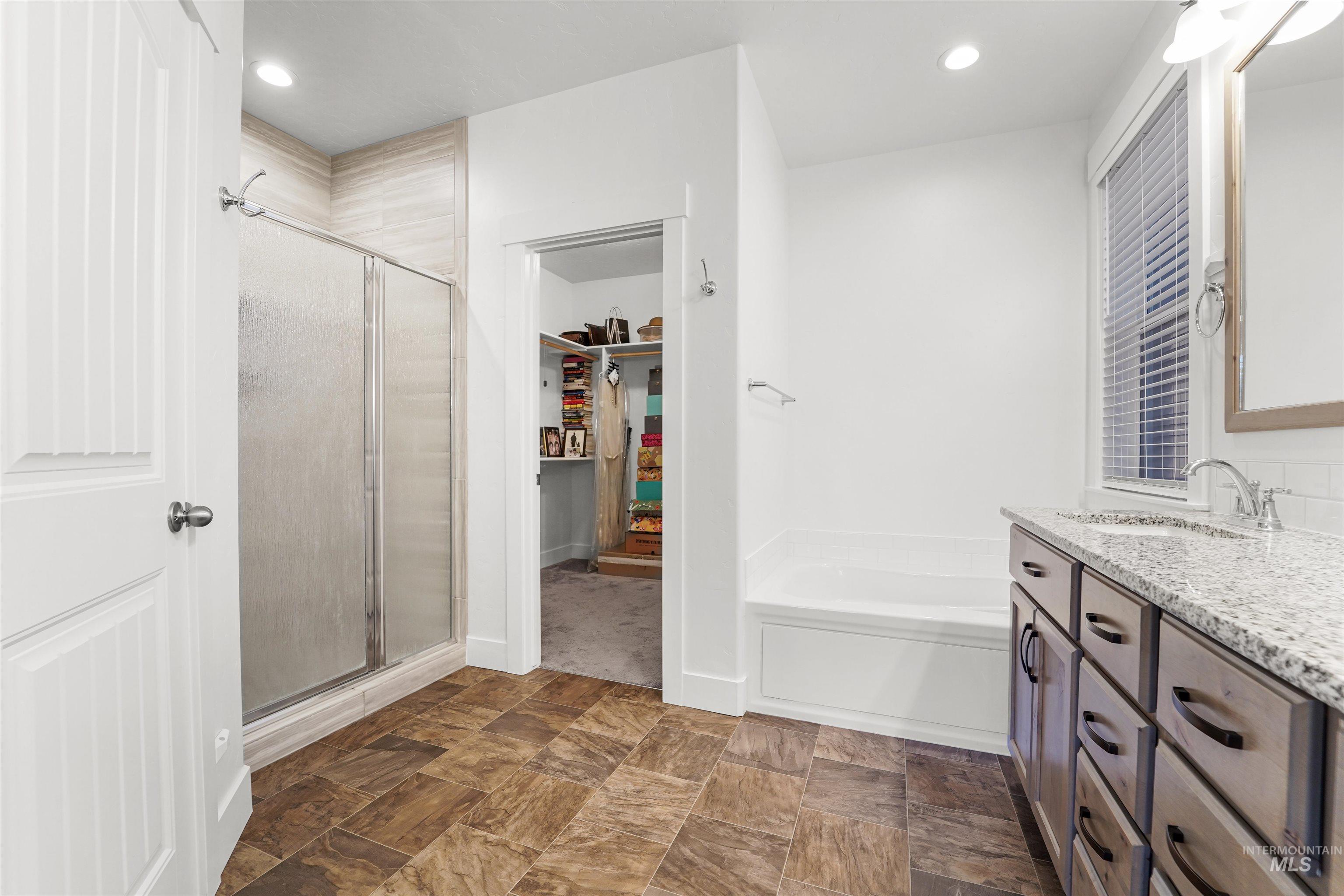 Full bathroom with a shower stall, vanity, a garden tub, a walk in closet, and recessed lighting