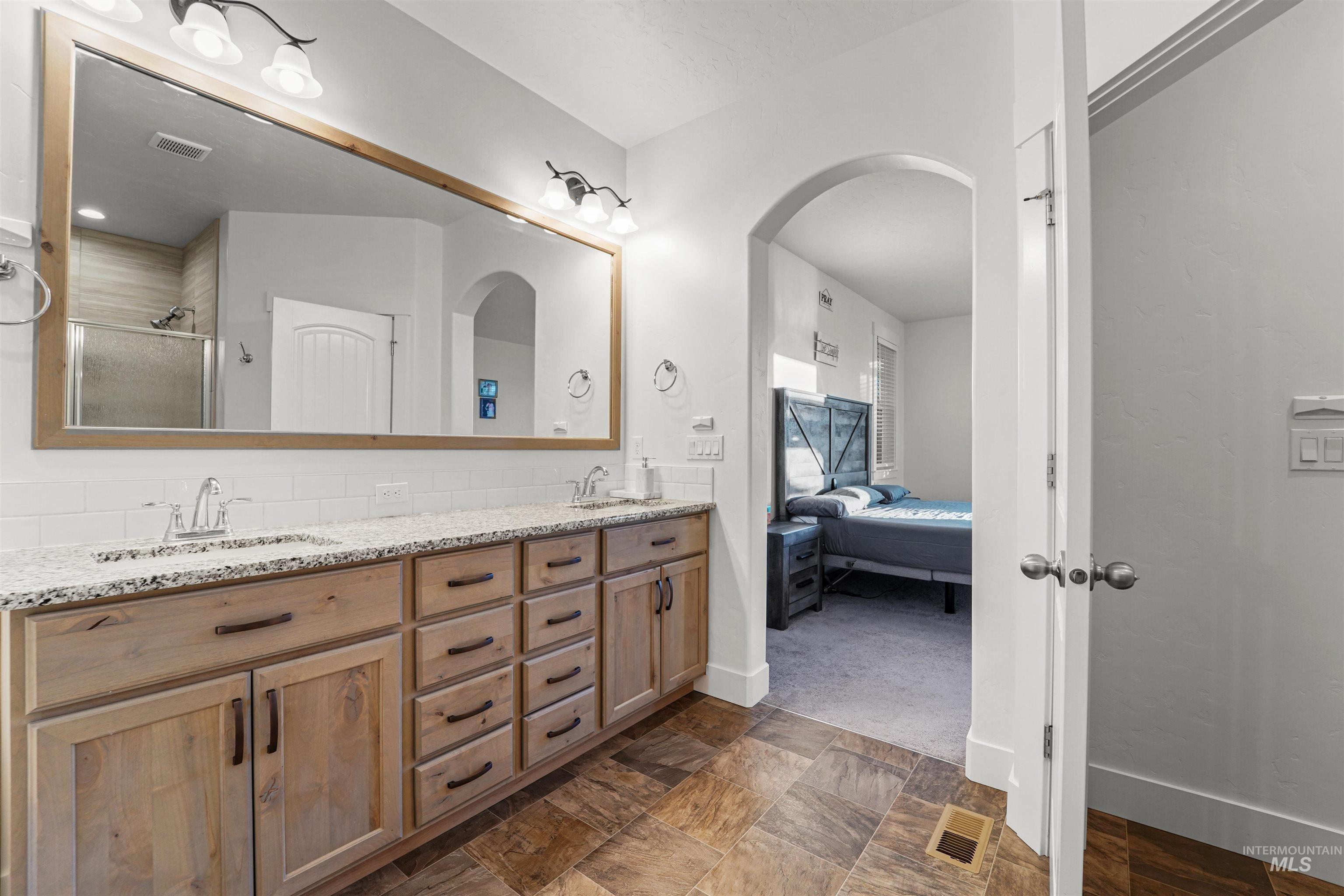 Ensuite bathroom with double vanity, a stall shower, dark stone finish floors, and tasteful backsplash