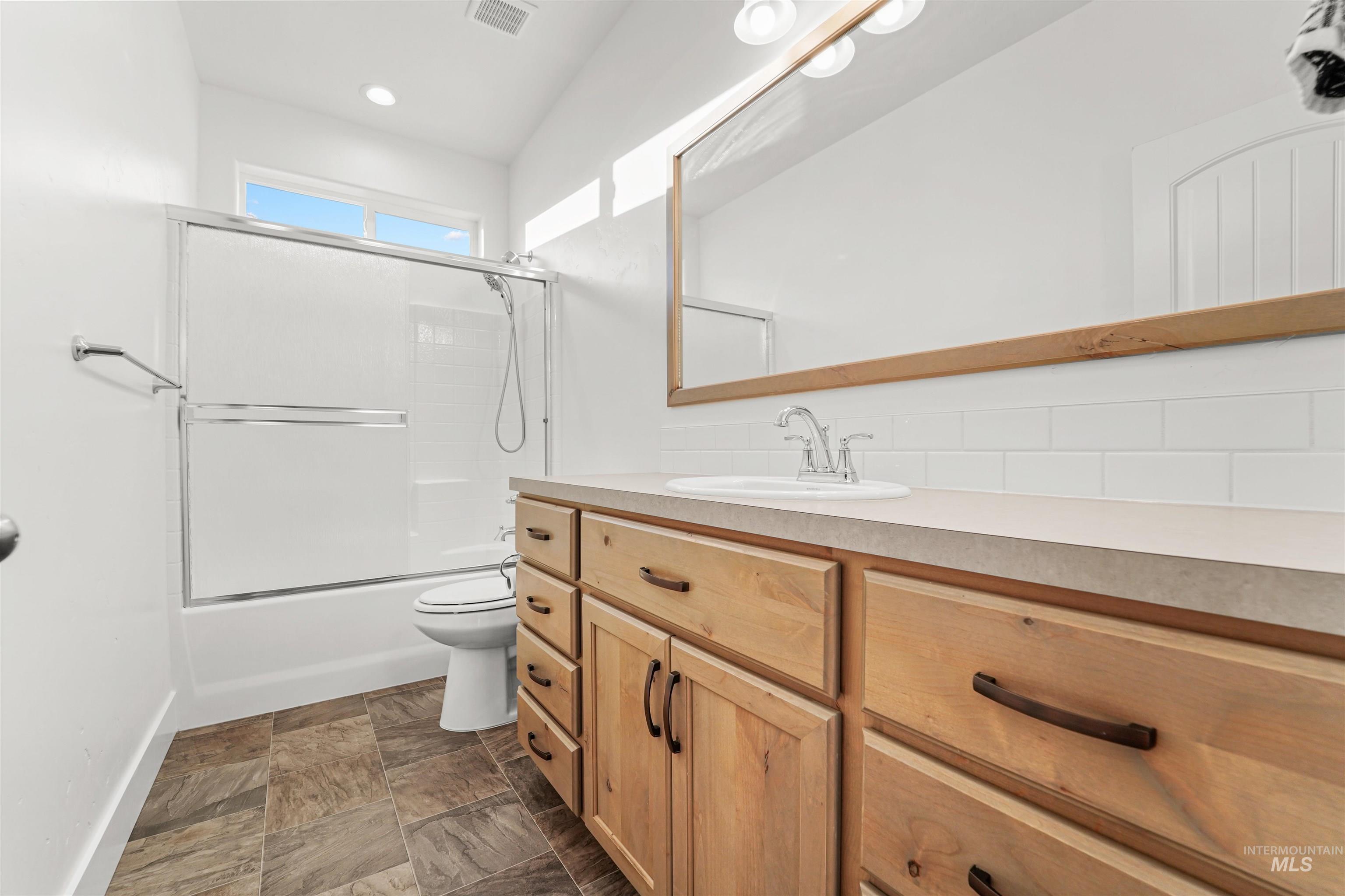 Full bath with shower / bath combination with glass door, vanity, tasteful backsplash, and dark stone finish floors