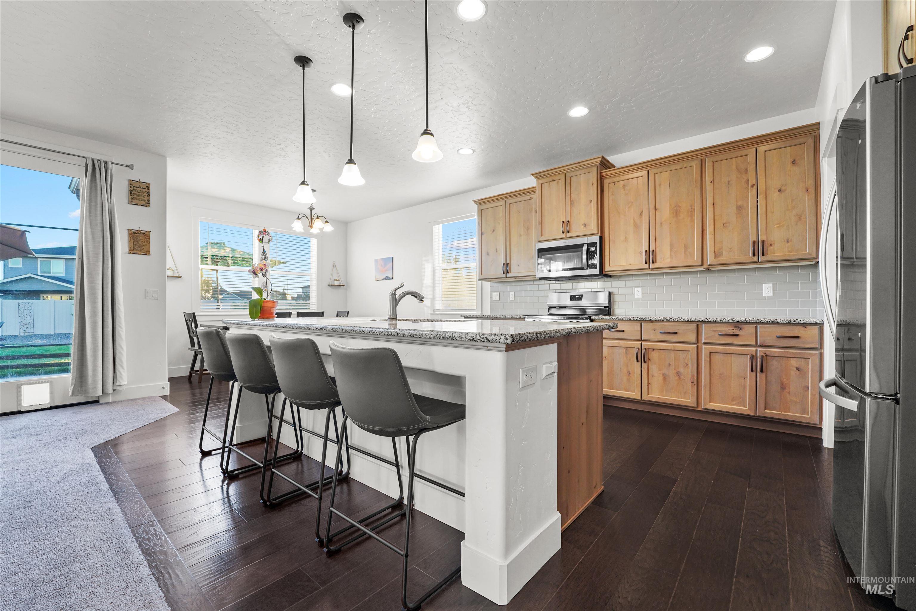 Kitchen with light stone counters, decorative backsplash, appliances with stainless steel finishes, a kitchen breakfast bar, and dark wood-type flooring