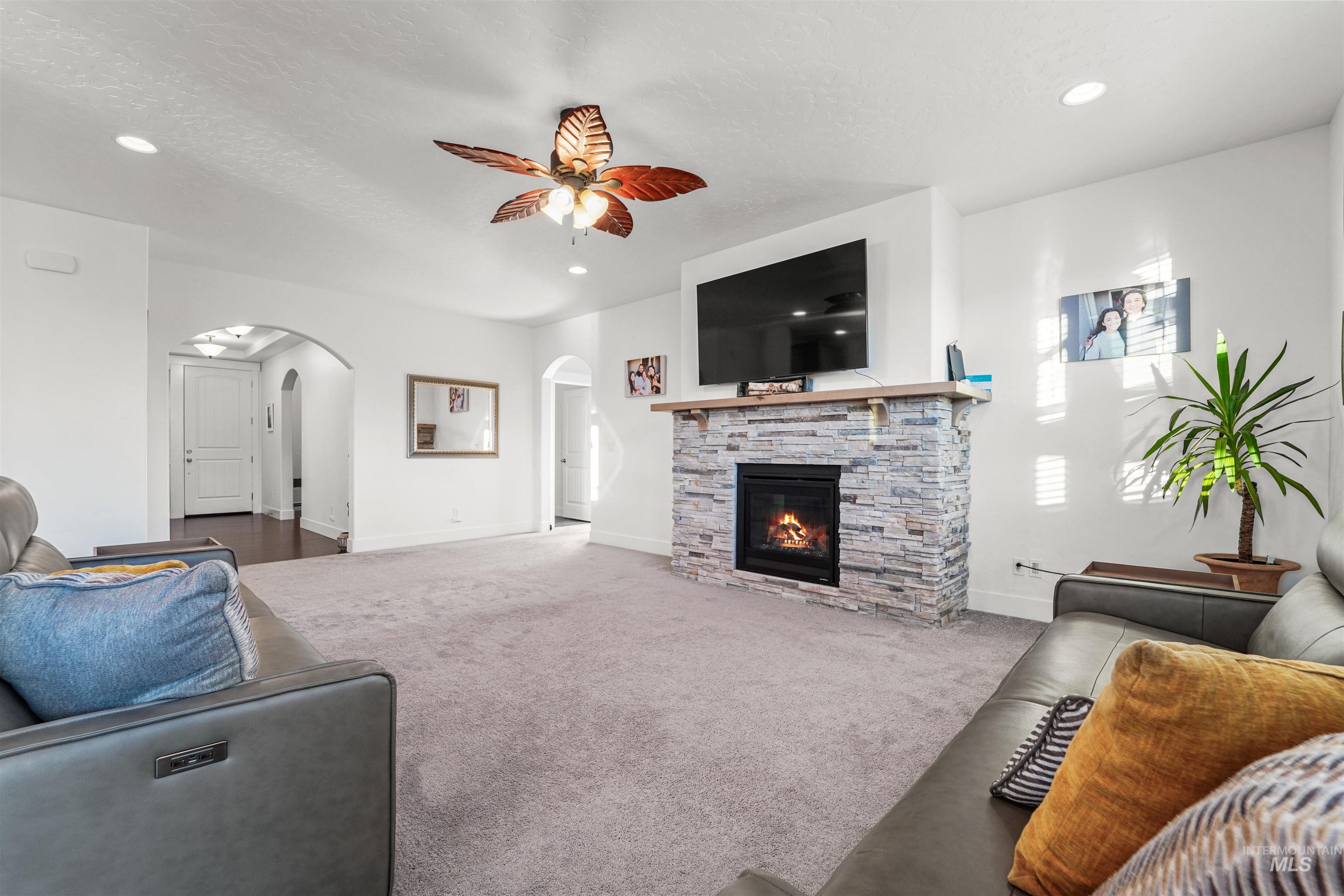 Living area featuring carpet floors, recessed lighting, a ceiling fan, a stone fireplace, and a textured ceiling
