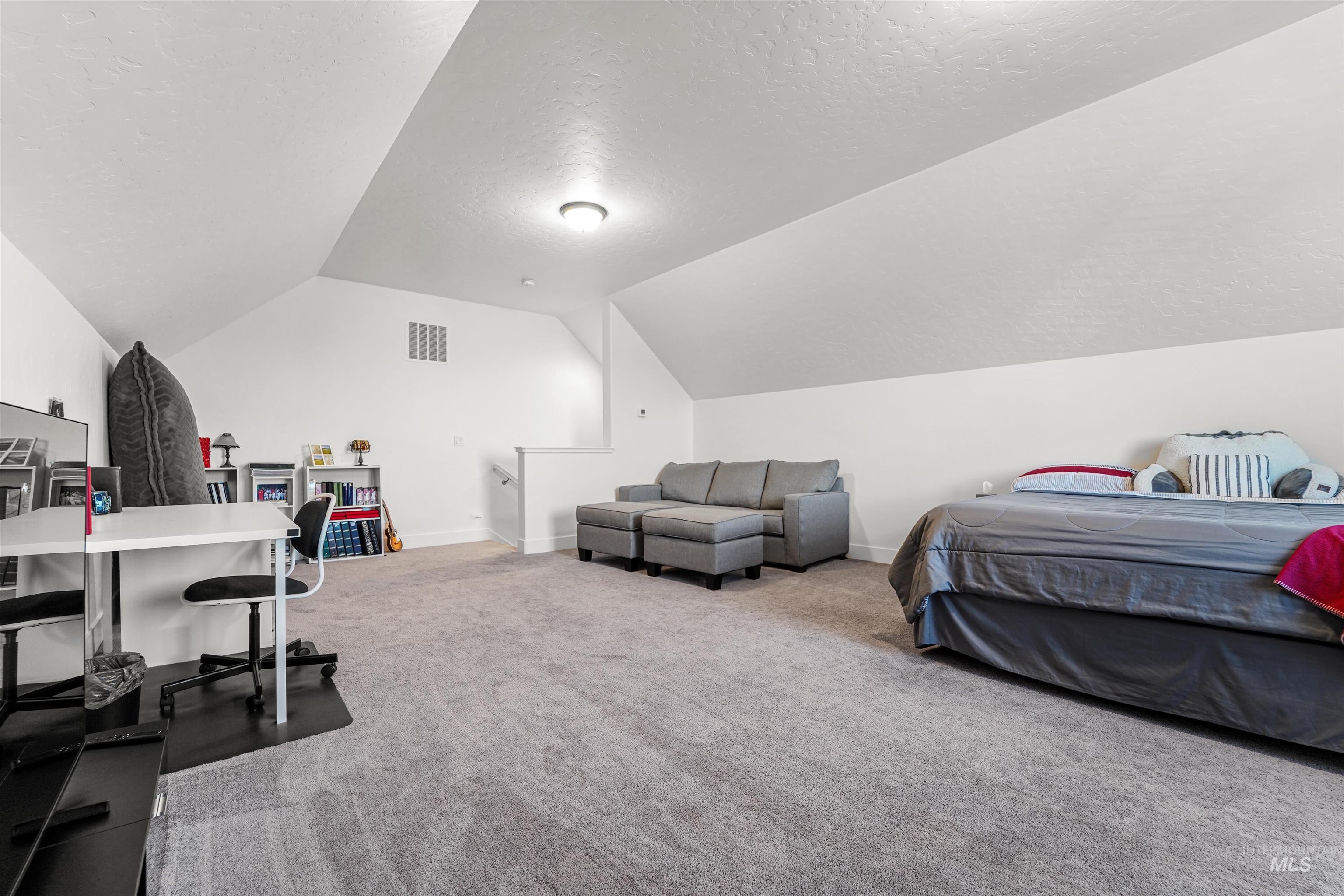 Bedroom featuring a textured ceiling, light colored carpet, and lofted ceiling