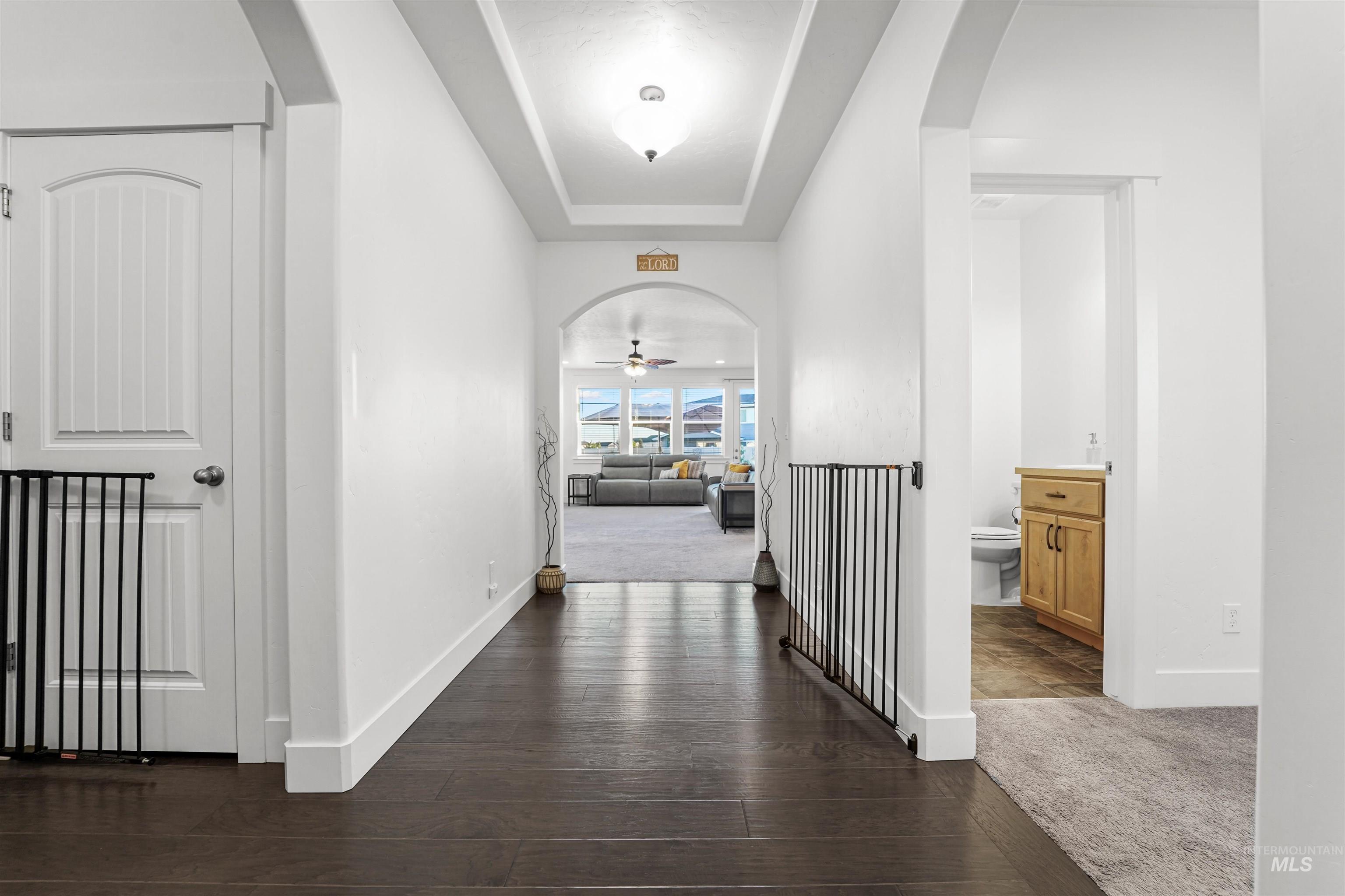 Hallway featuring arched walkways, a tray ceiling, and dark colored carpet