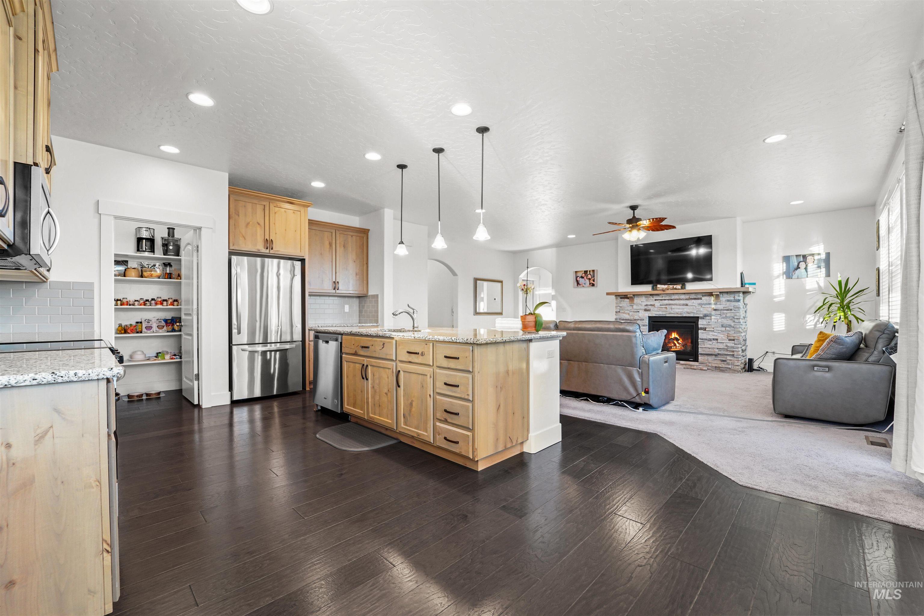 Kitchen featuring light stone countertops, pendant lighting, a fireplace, appliances with stainless steel finishes, and open floor plan