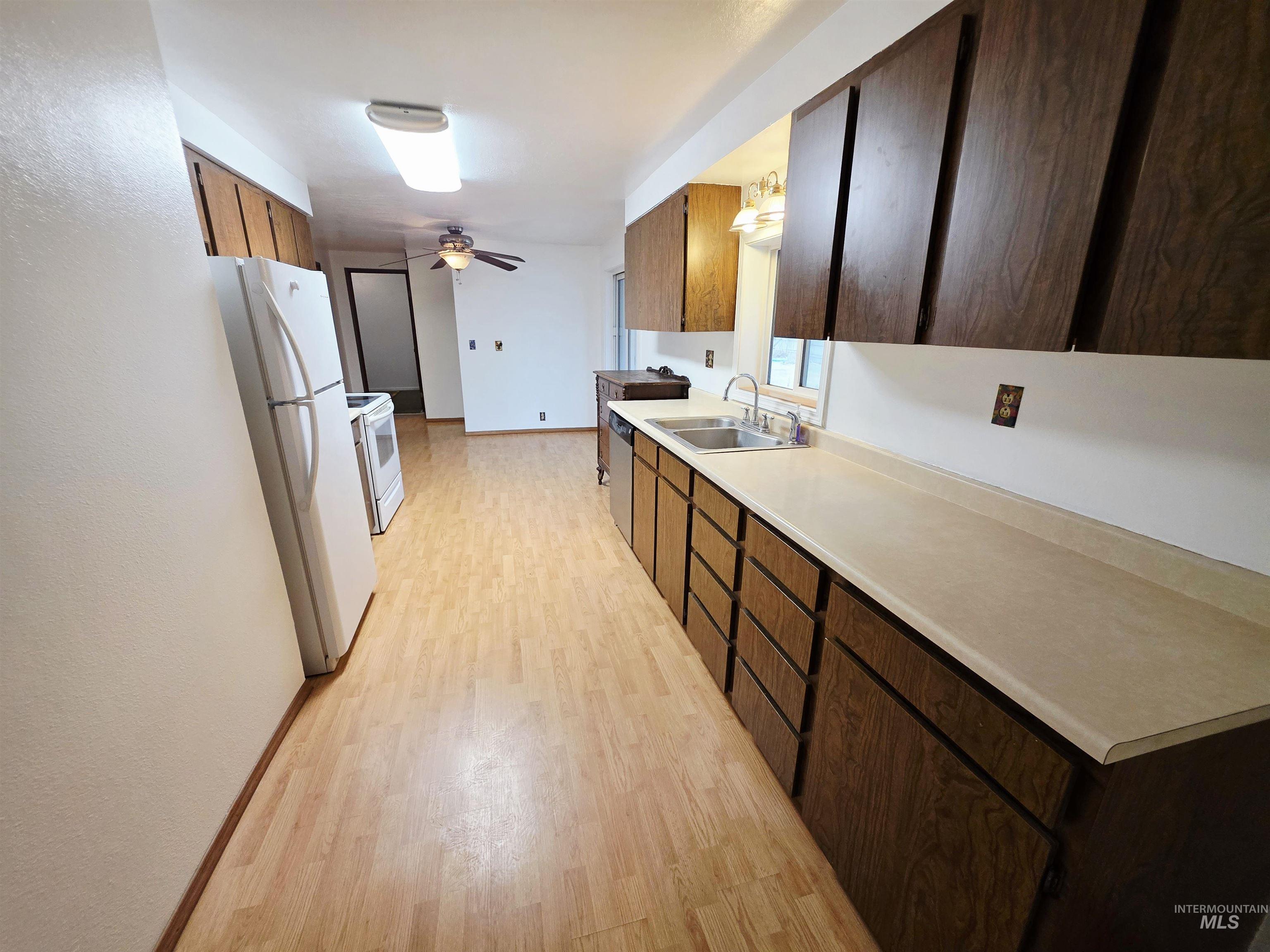 Kitchen featuring light countertops, white appliances, light wood-type flooring, a ceiling fan, and dark brown cabinets