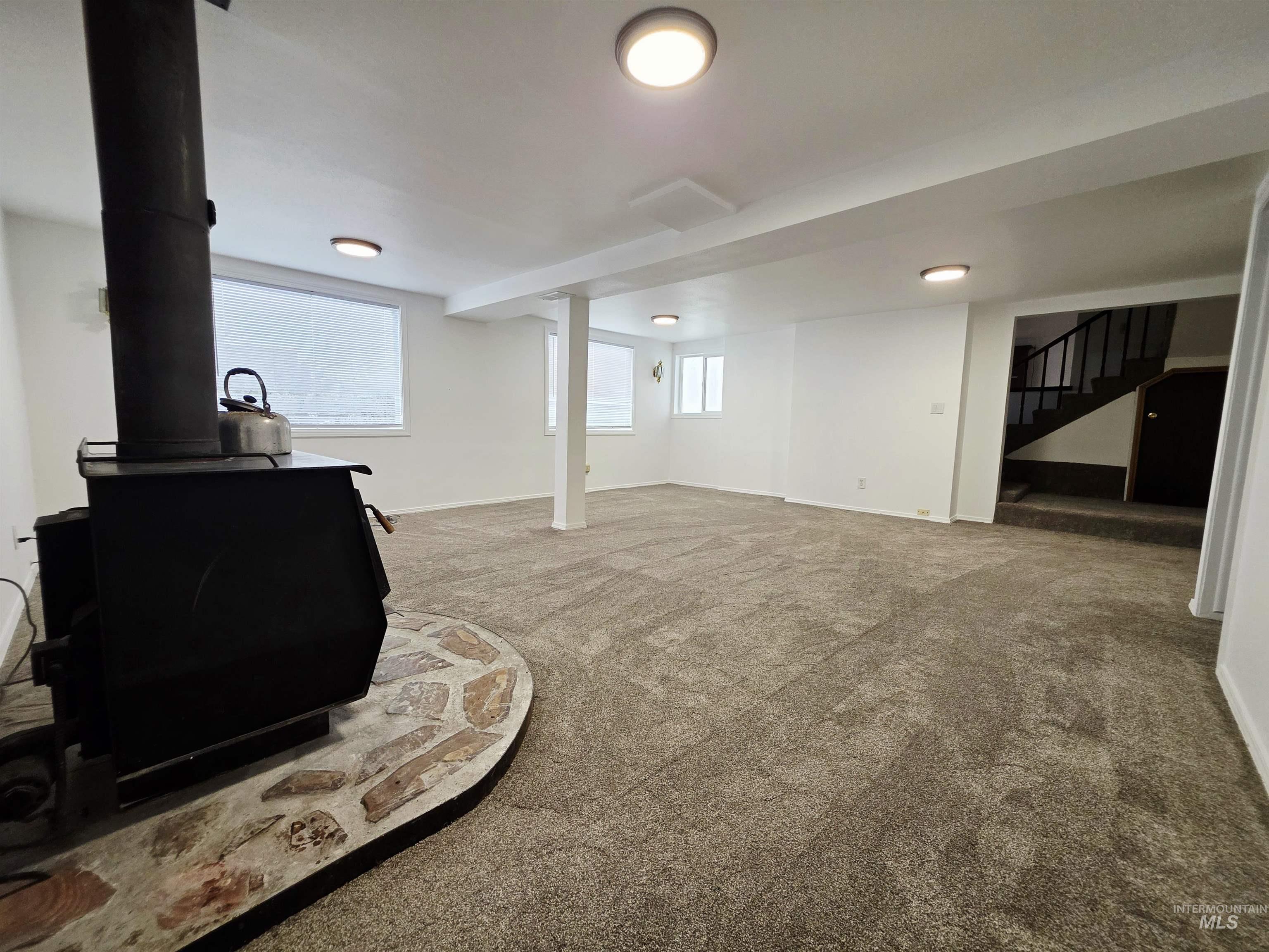 Below grade area featuring carpet flooring, a wood stove, and stairway