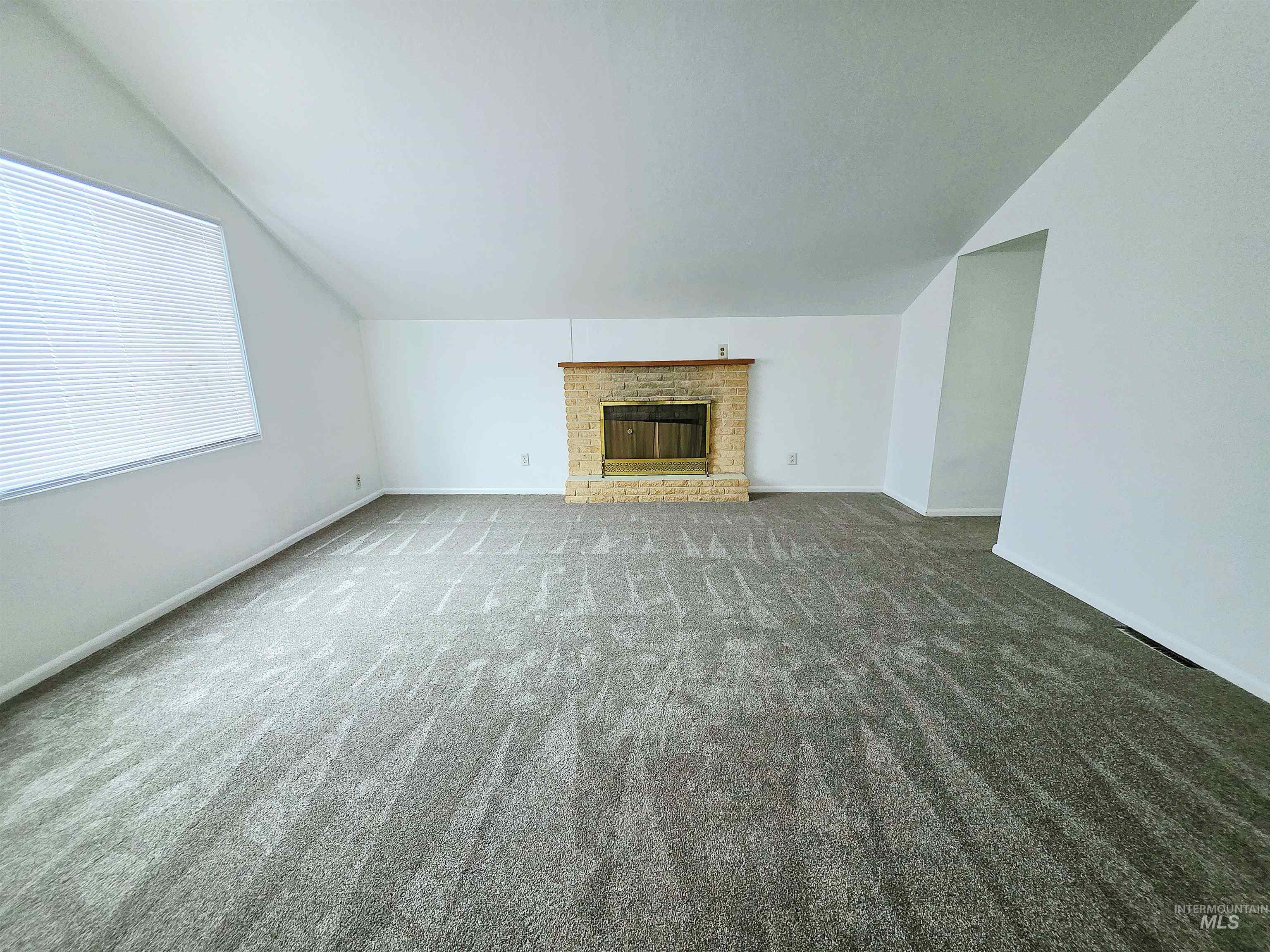 Unfurnished living room featuring lofted ceiling, a fireplace, and carpet