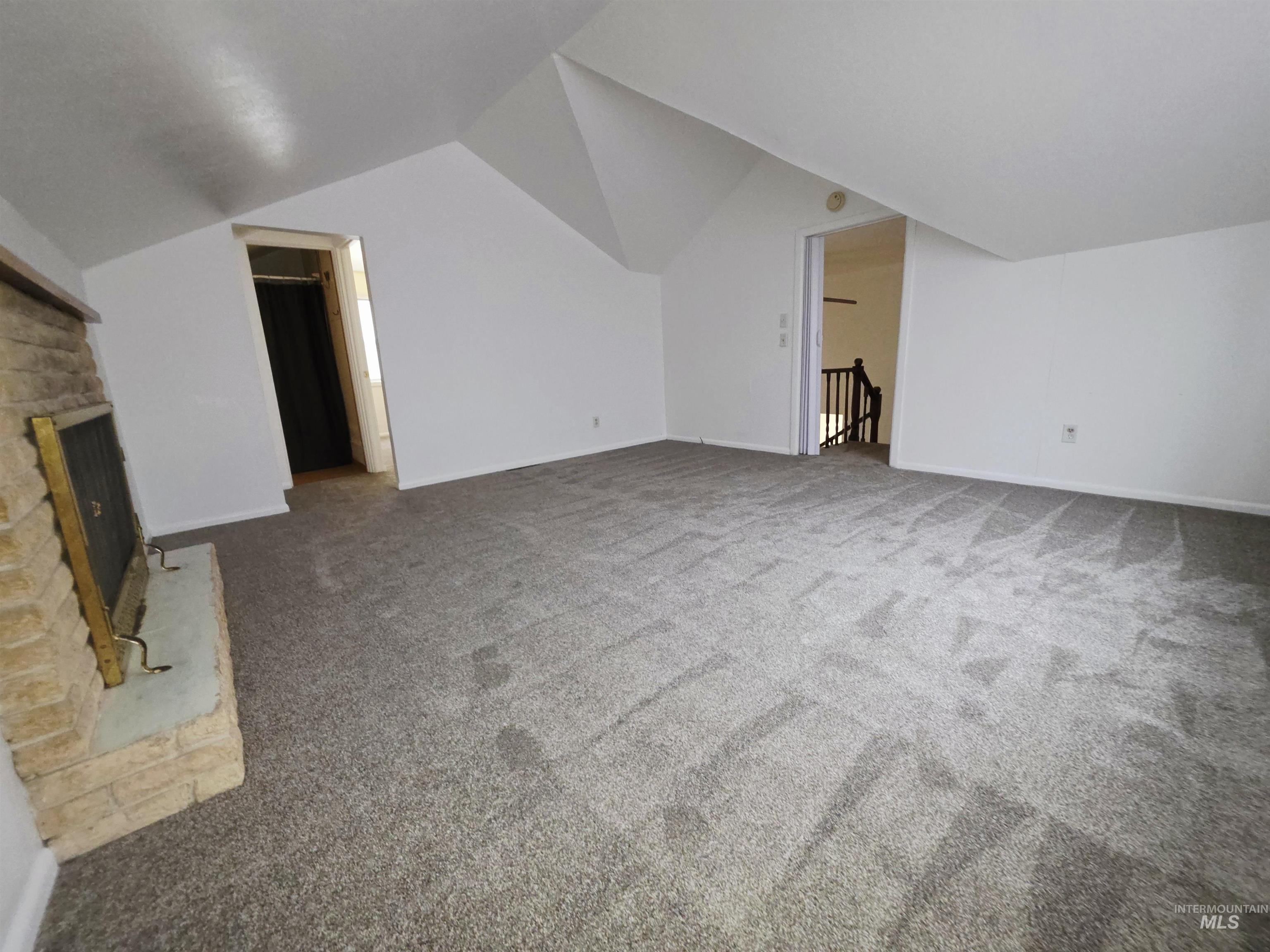 Additional living space with lofted ceiling, a fireplace with raised hearth, and carpet