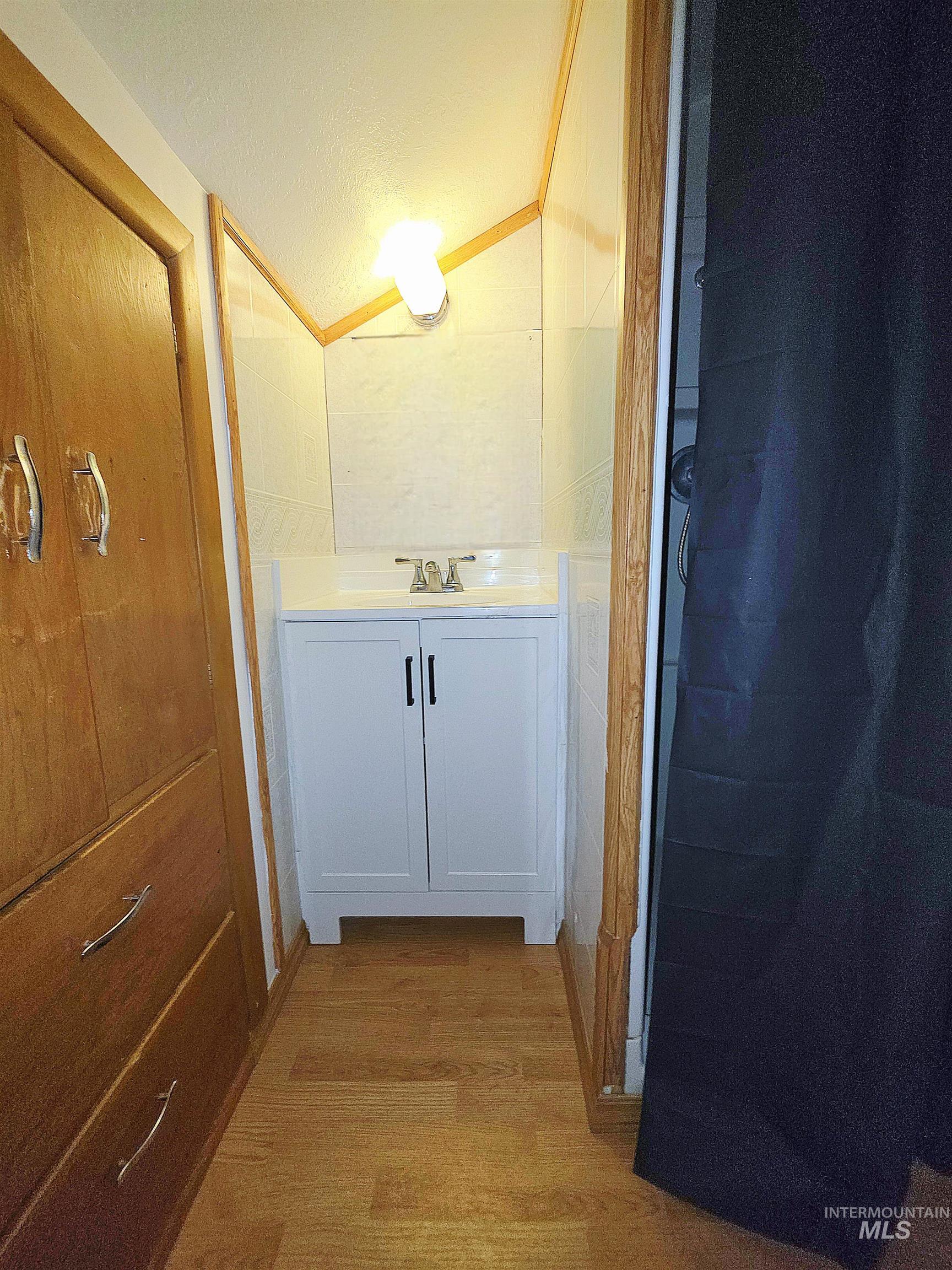 Half bath featuring vanity, light wood-type flooring, lofted ceiling, and a textured ceiling