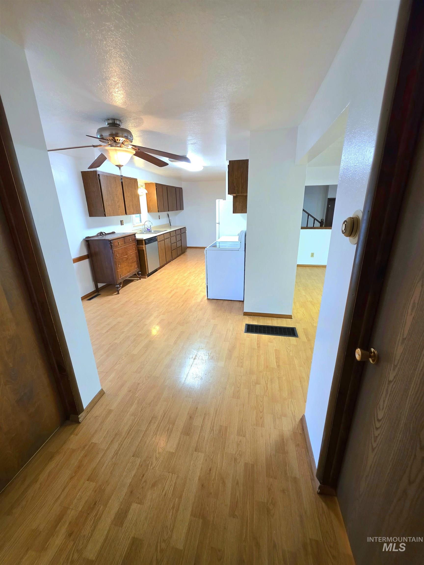 Kitchen featuring brown cabinets, white appliances, light countertops, light wood-type flooring, and a ceiling fan