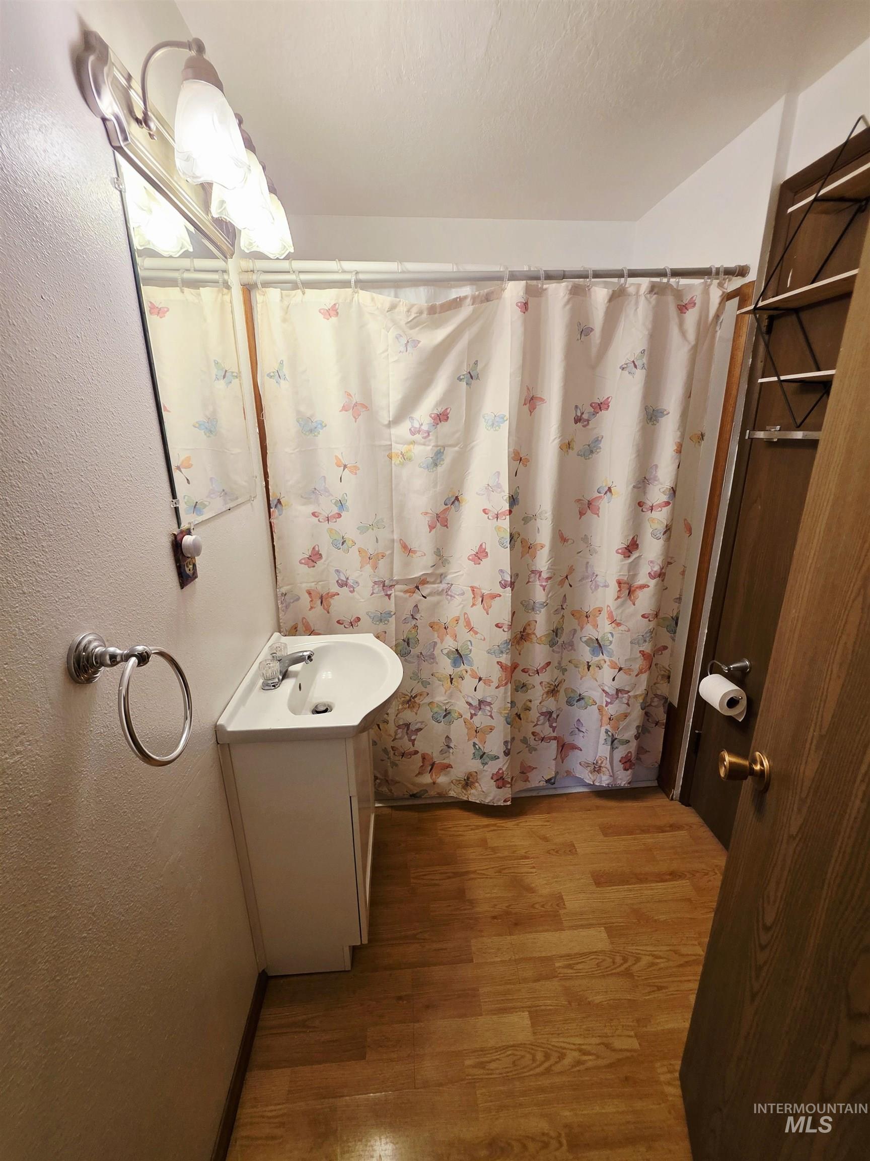 Full bath with vanity, a shower with curtain, light wood-style flooring, and a textured wall