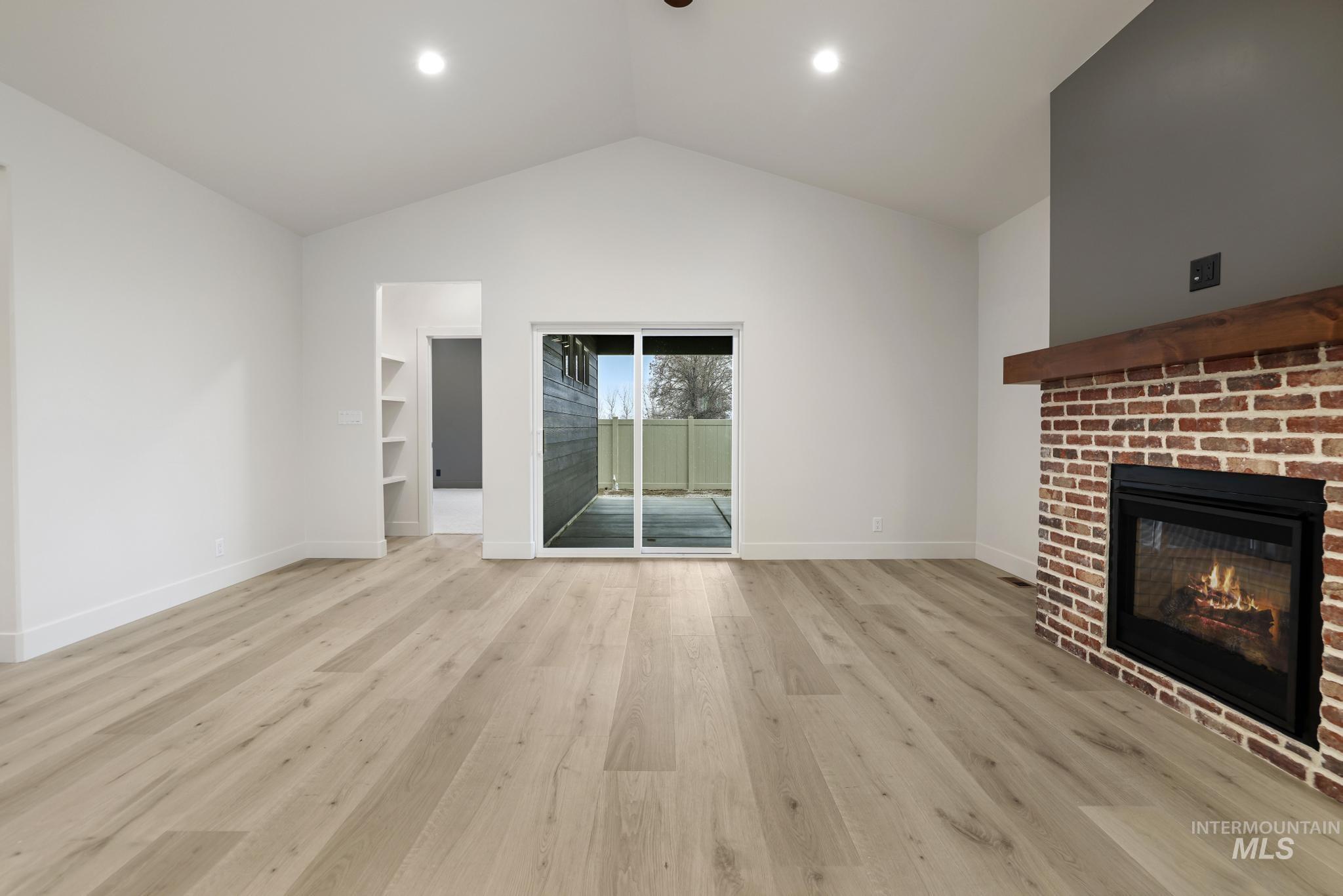 Unfurnished living room featuring light wood-type flooring, vaulted ceiling, and a brick fireplace