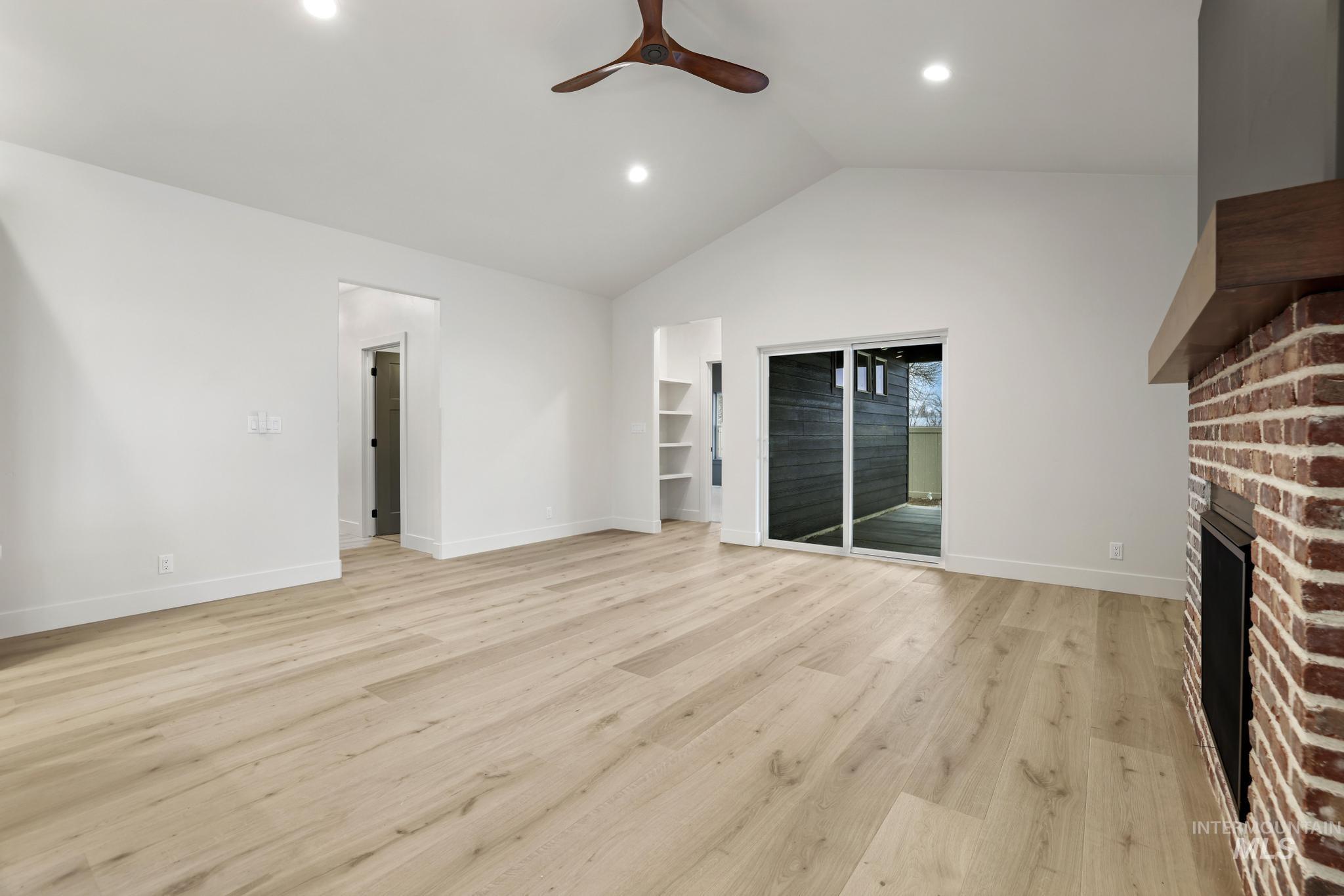 Unfurnished living room with light wood-type flooring, lofted ceiling, a brick fireplace, a ceiling fan, and recessed lighting