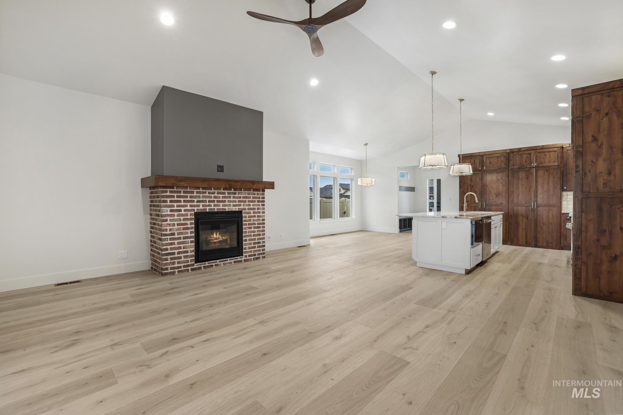 Unfurnished living room featuring a fireplace, light wood-style flooring, ceiling fan, recessed lighting, and high vaulted ceiling