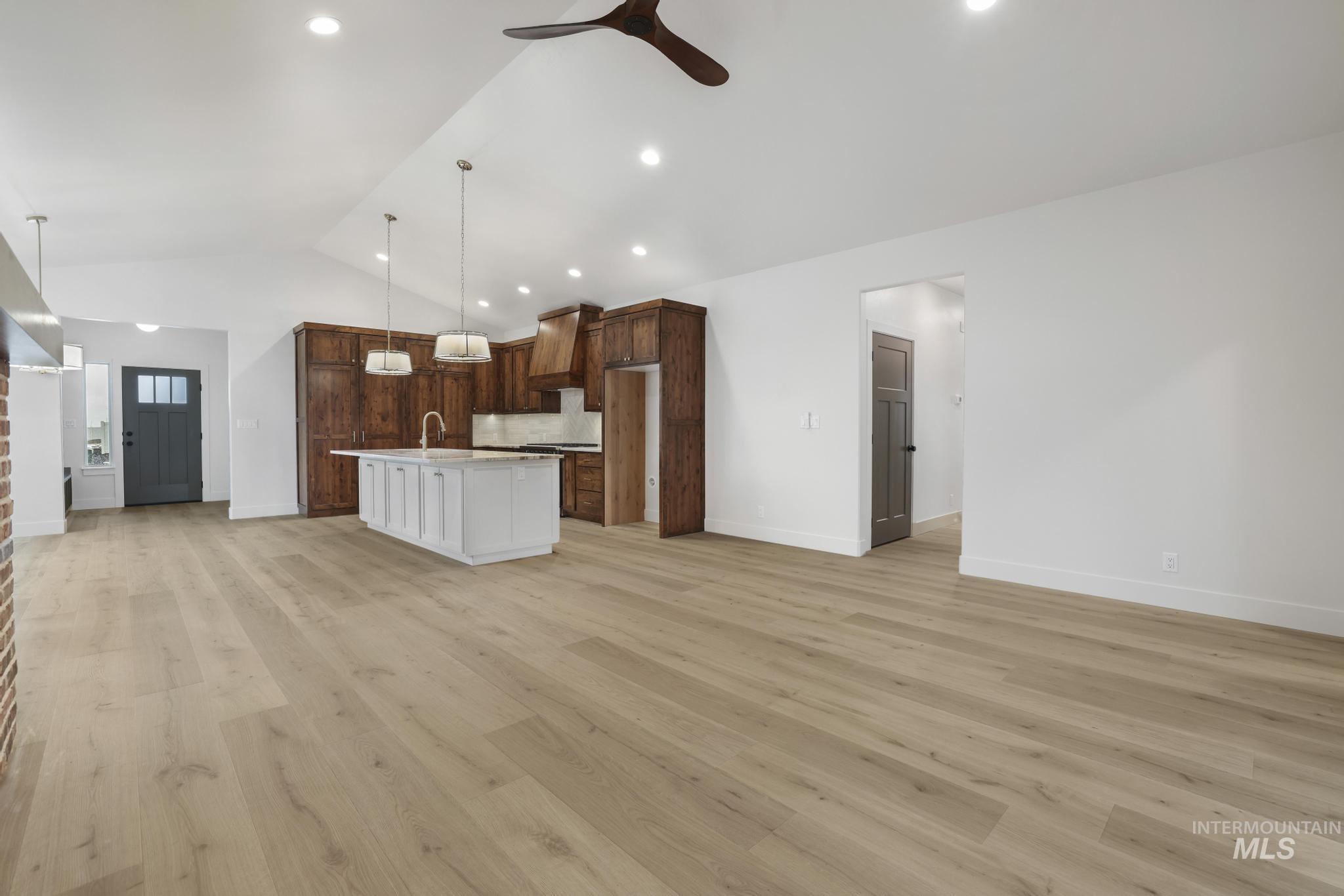 Kitchen with open floor plan, light wood-style floors, a center island with sink, hanging light fixtures, and ceiling fan