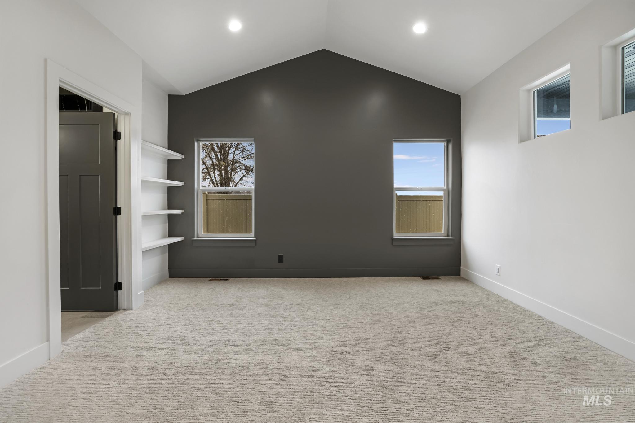 Spare room featuring vaulted ceiling, light carpet, and plenty of natural light