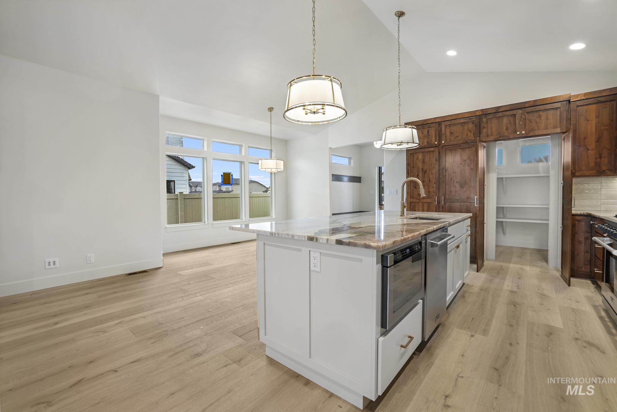 Kitchen featuring light stone counters, light wood-style flooring, decorative light fixtures, a kitchen island with sink, and lofted ceiling