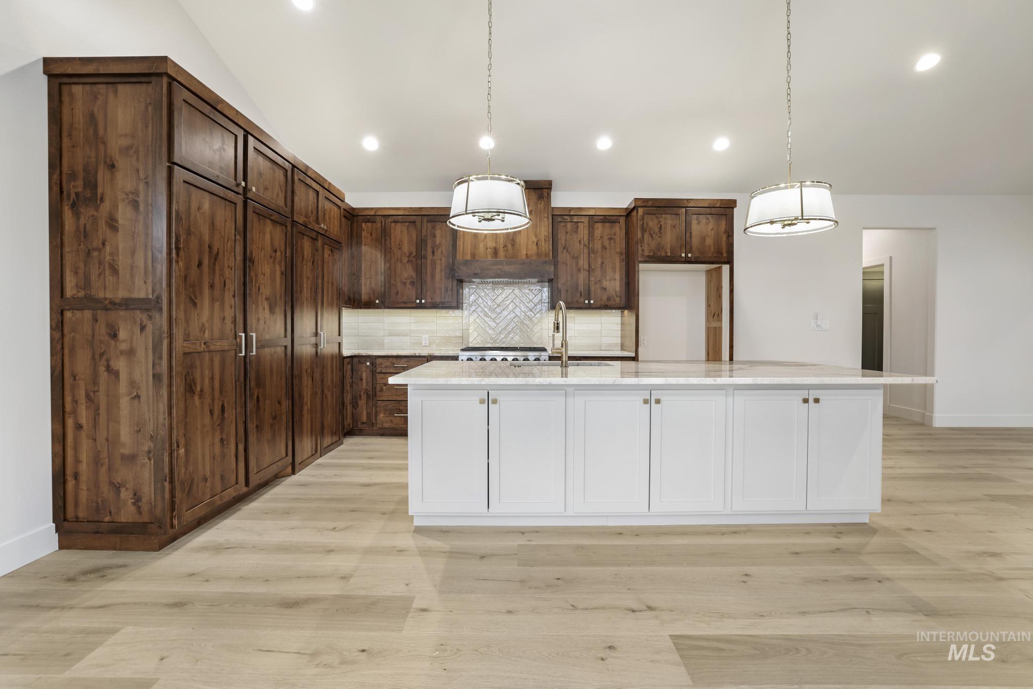 Kitchen with tasteful backsplash, hanging light fixtures, white cabinets, an island with sink, and light stone countertops