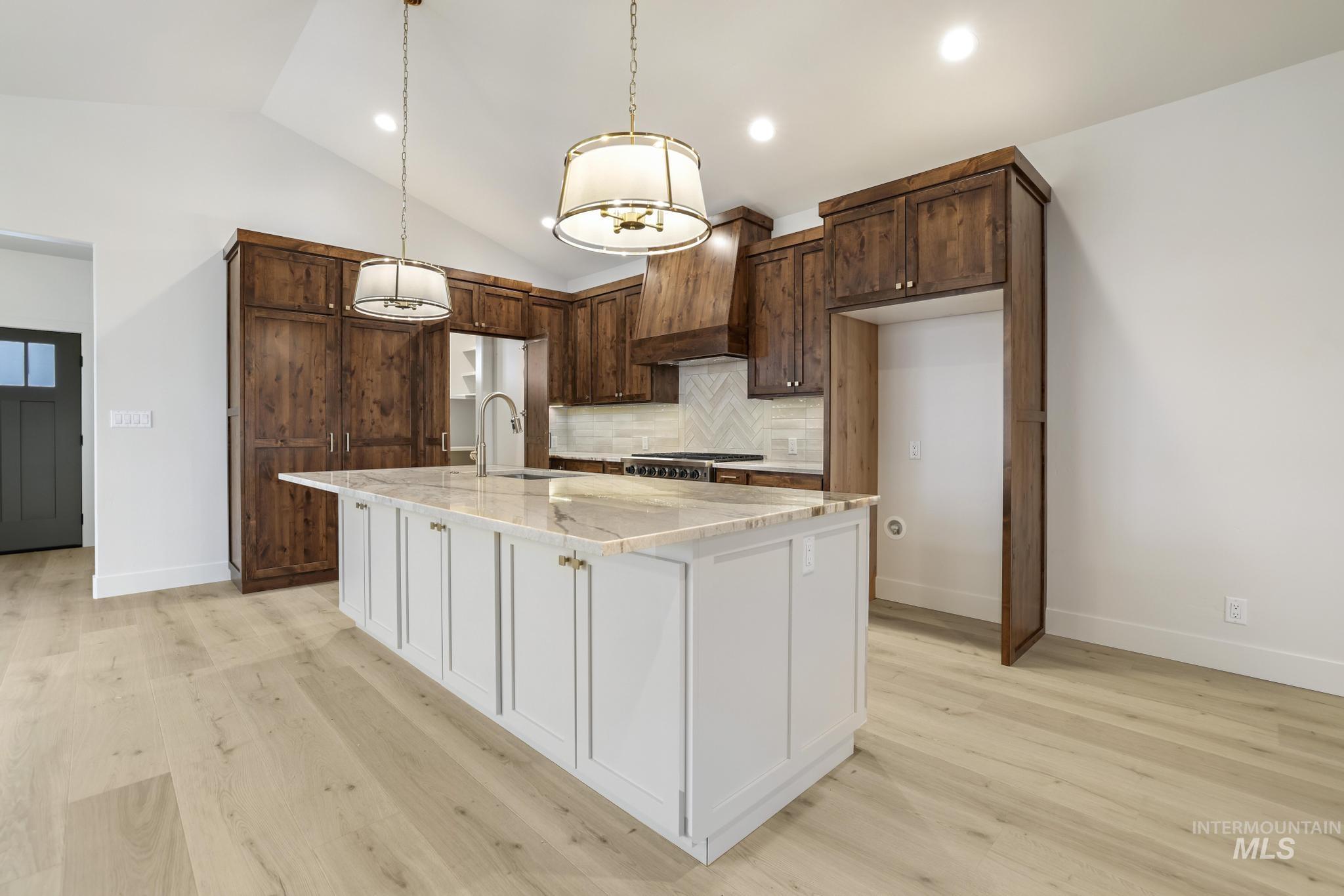 Kitchen with white cabinetry, premium range hood, light stone countertops, vaulted ceiling, and backsplash