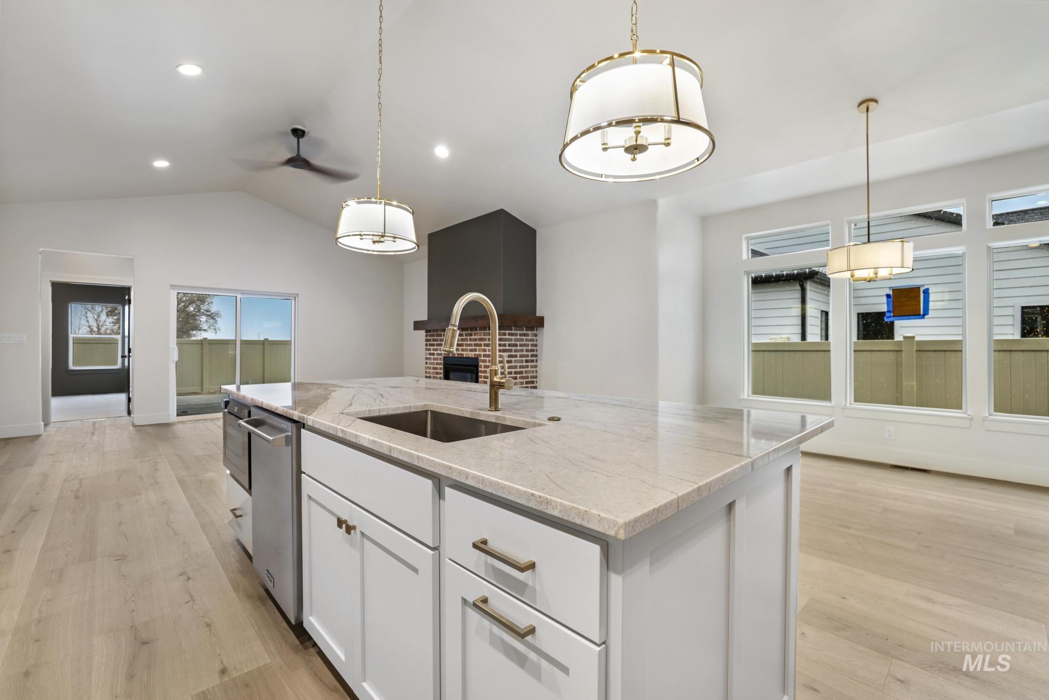 Kitchen with white cabinetry, light stone counters, hanging light fixtures, an island with sink, and light wood-style floors