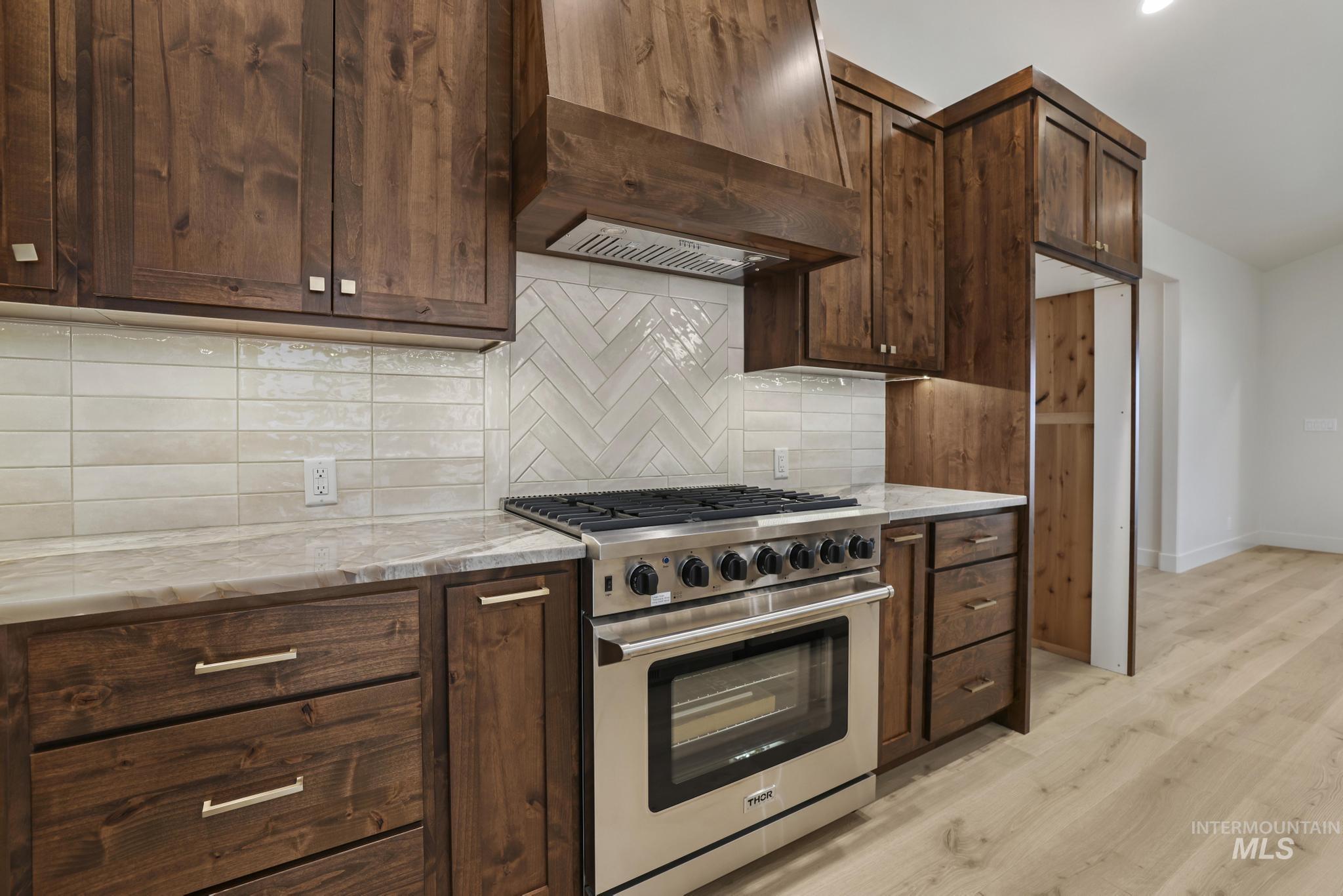 Kitchen with high end range, custom range hood, light stone counters, and dark brown cabinets