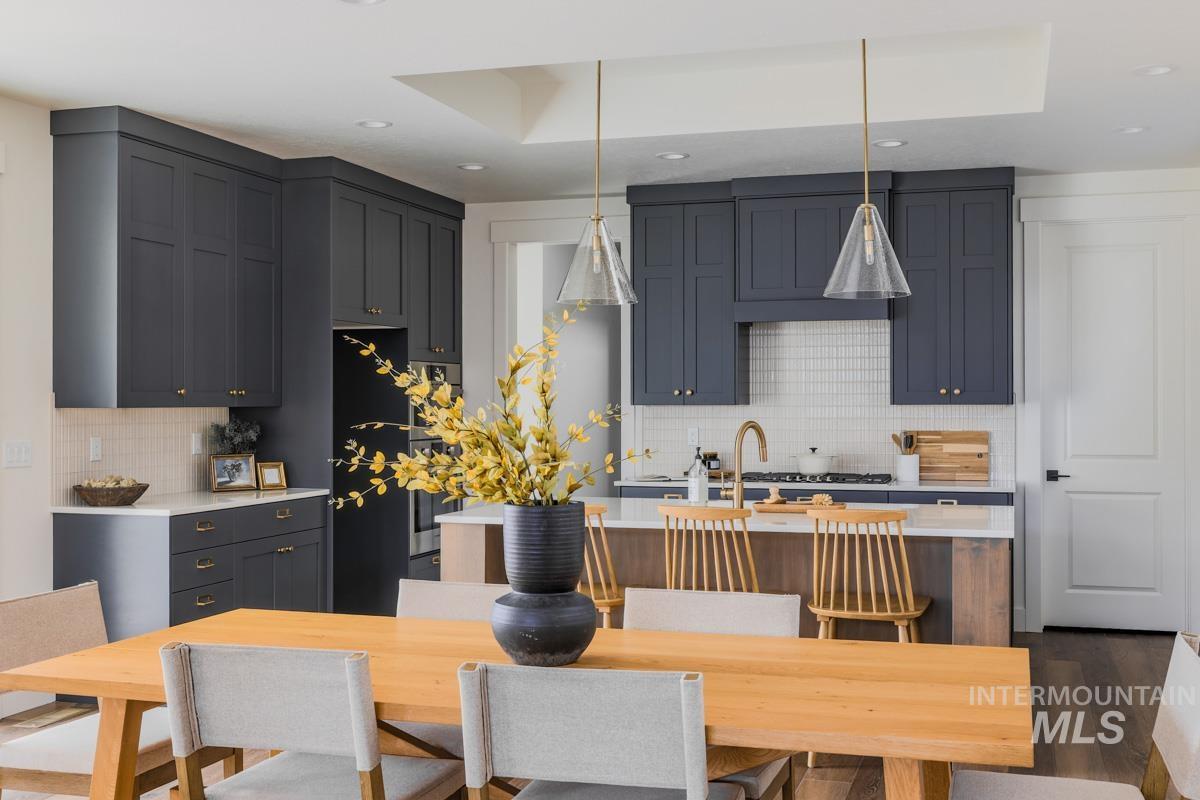 Kitchen with a center island with sink, pendant lighting, backsplash, black refrigerator, and light stone counters