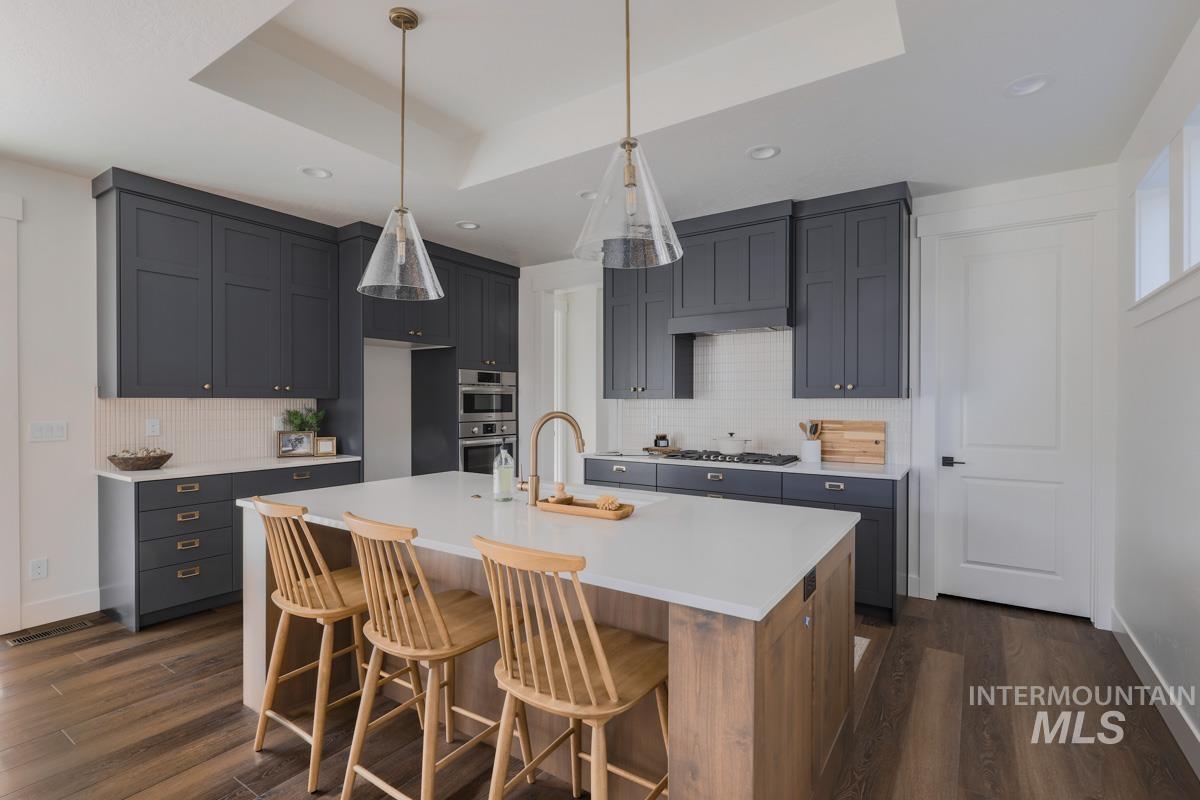 Kitchen with a raised ceiling, dark wood-style floors, a kitchen bar, decorative light fixtures, and decorative backsplash