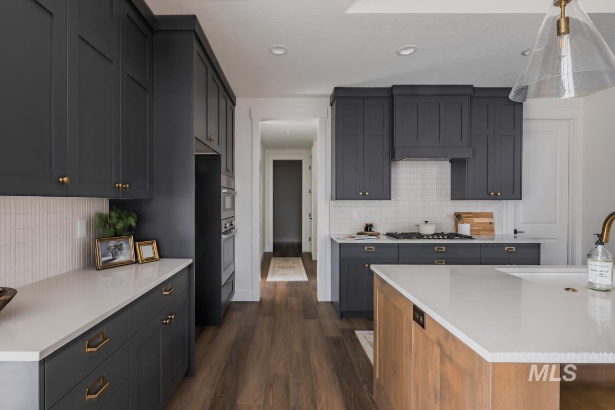 Kitchen with dark wood finished floors, backsplash, hanging light fixtures, light stone countertops, and recessed lighting