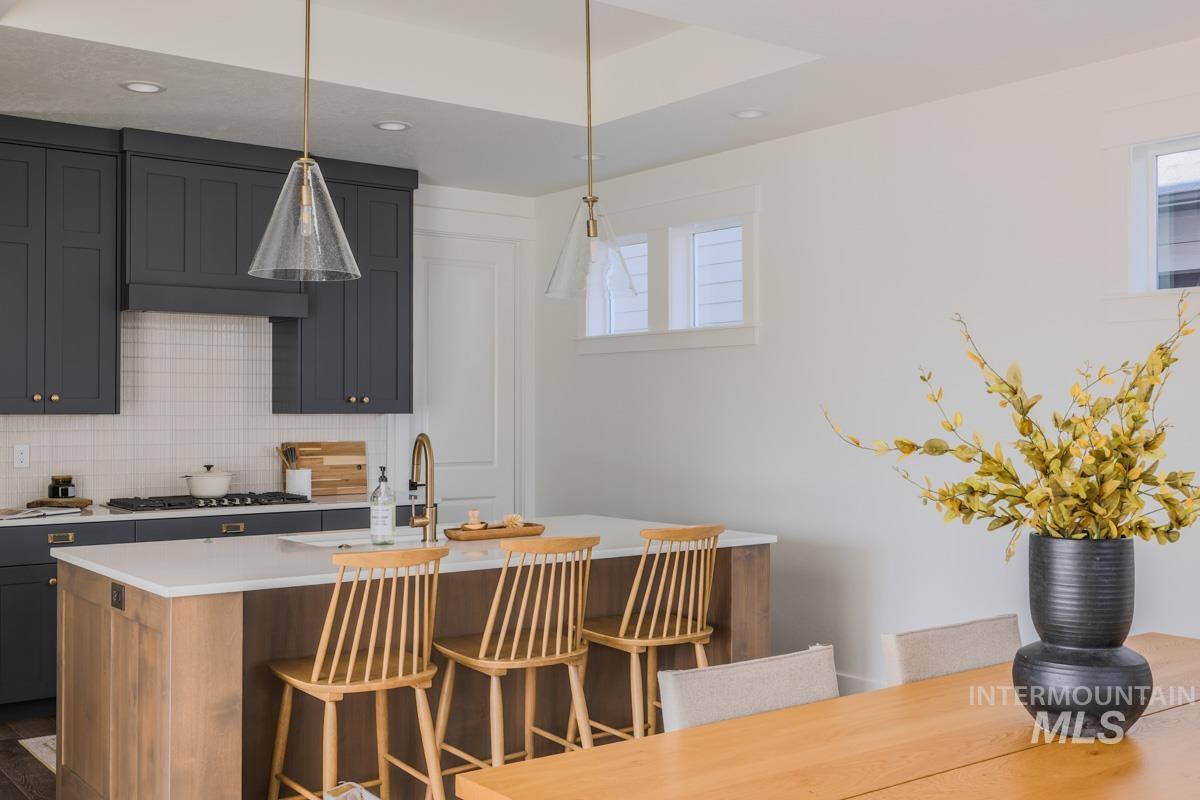Kitchen featuring a breakfast bar, decorative light fixtures, decorative backsplash, a kitchen island with sink, and light stone counters