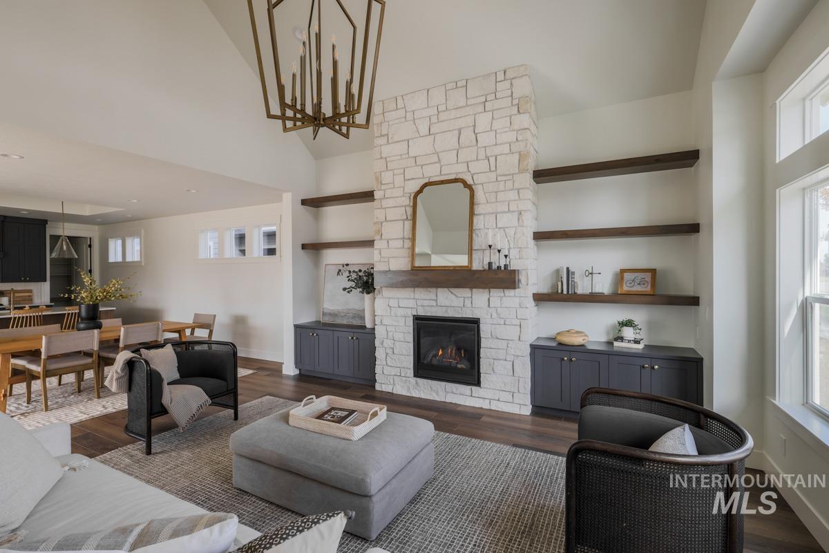 Living room featuring dark wood-style floors, a stone fireplace, a high ceiling, and a chandelier