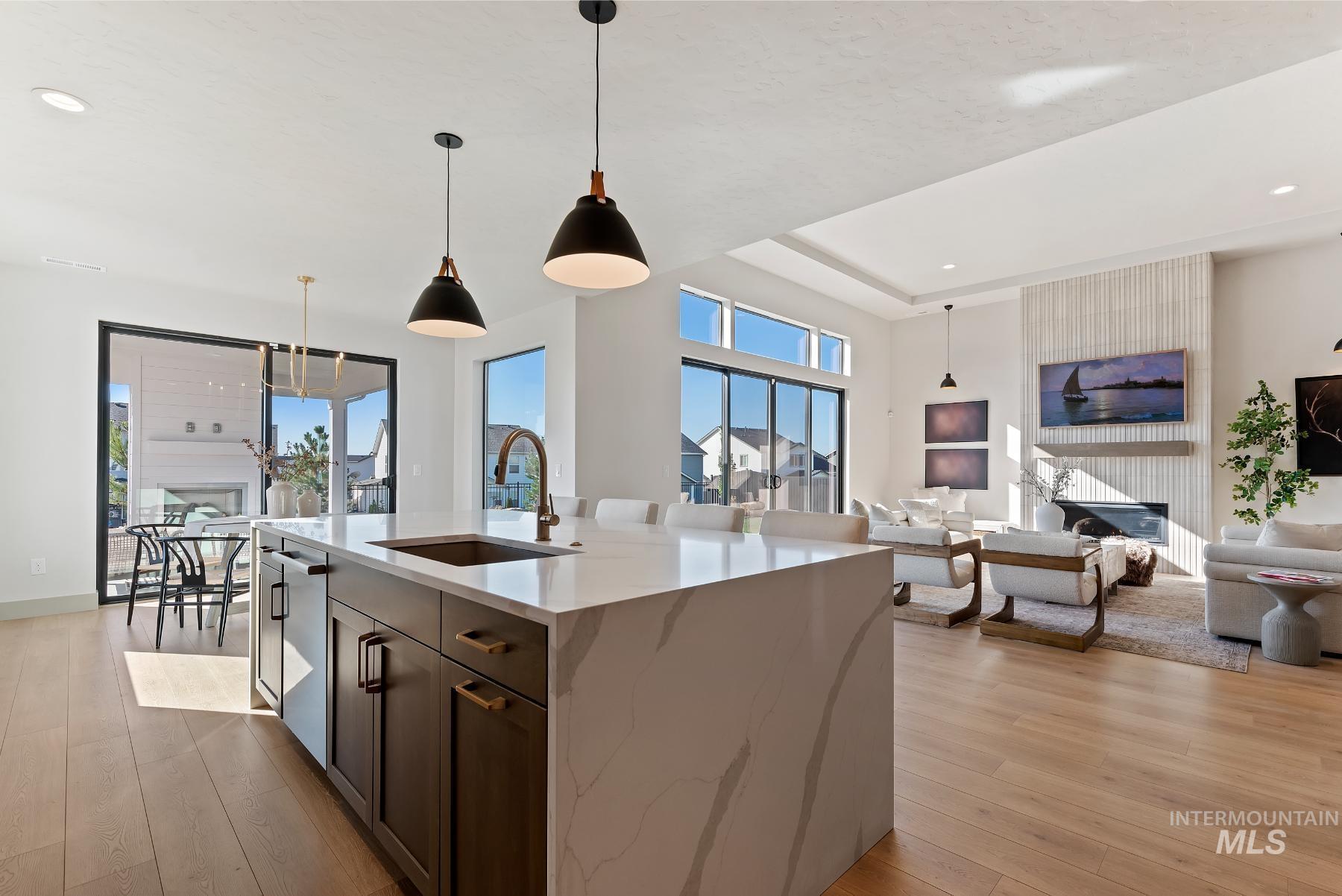 Kitchen with open floor plan, hanging light fixtures, light stone counters, light wood finished floors, and recessed lighting