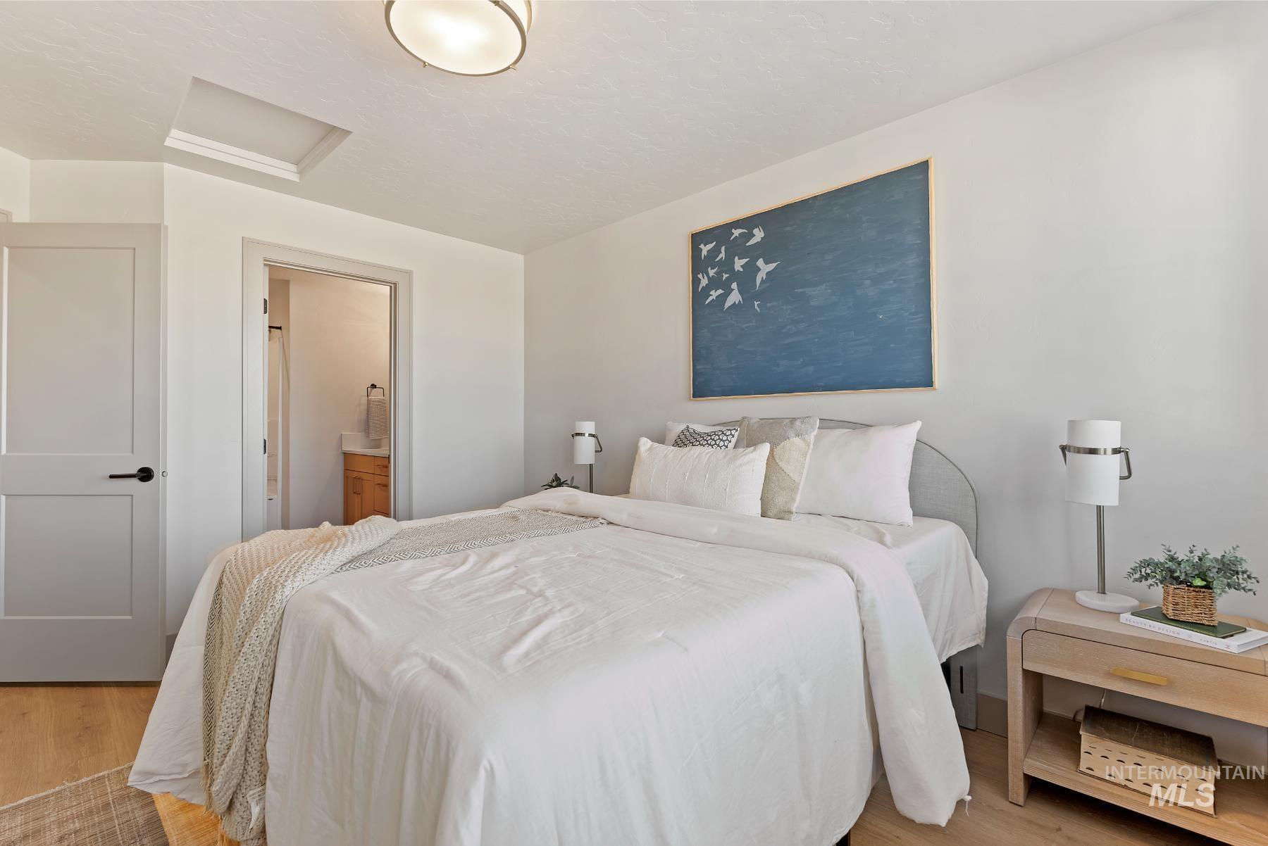 Bedroom with attic access, light wood-type flooring, and ensuite bath