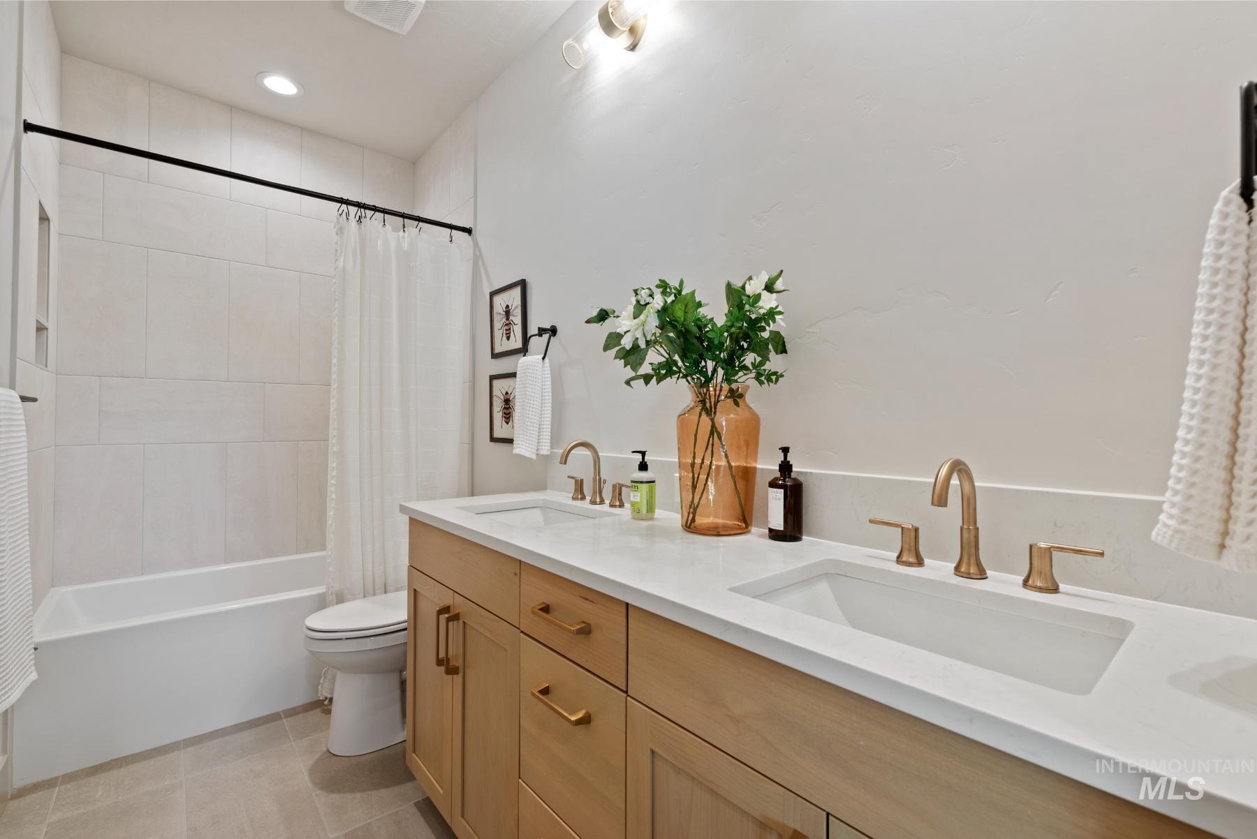 Bathroom featuring double vanity, shower / tub combo with curtain, and light tile patterned floors