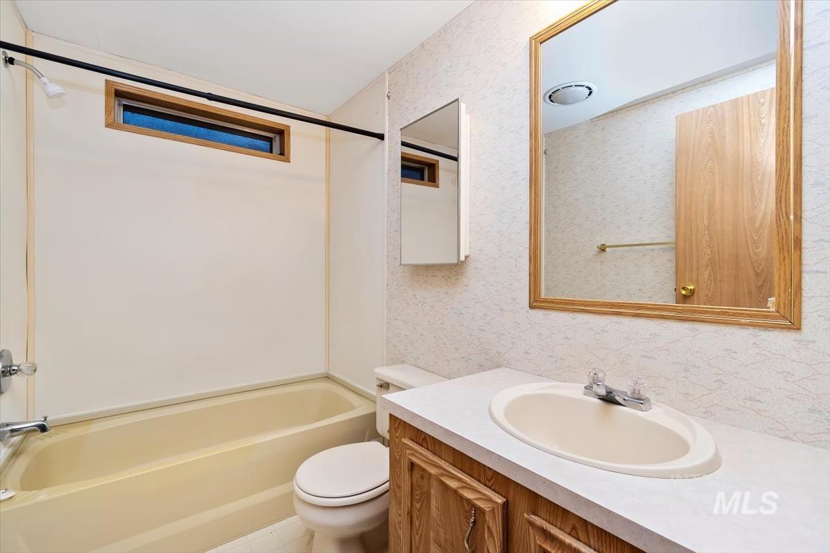 Bathroom featuring tub / shower combination, vanity, and wallpapered walls
