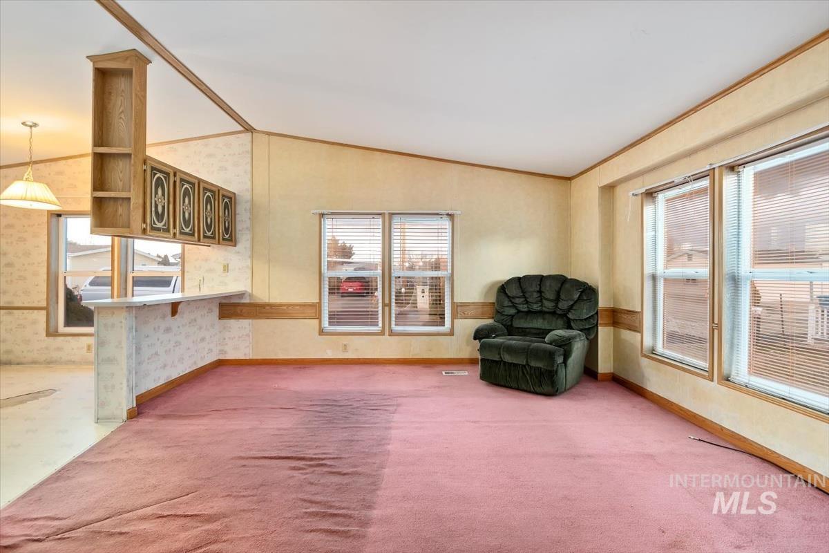 Sitting room with lofted ceiling, ornamental molding, plenty of natural light, and wallpapered walls