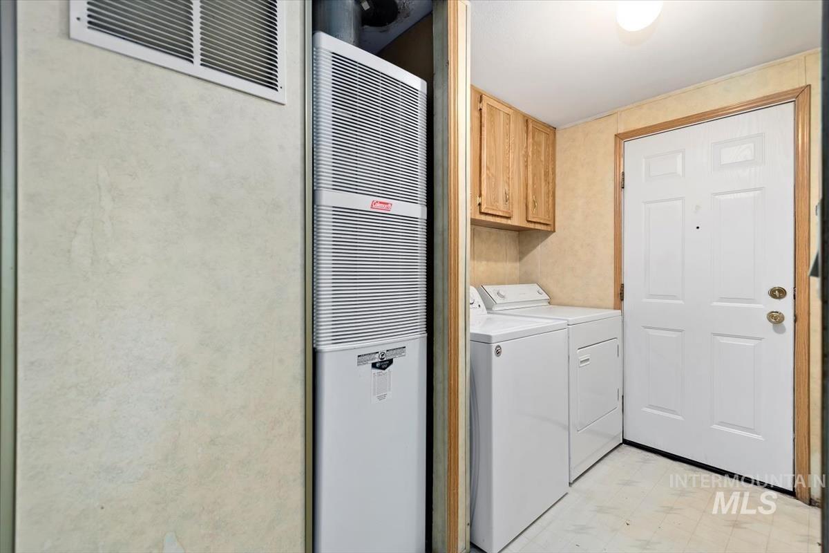 Washroom featuring light floors, a heating unit, washing machine and clothes dryer, and cabinet space